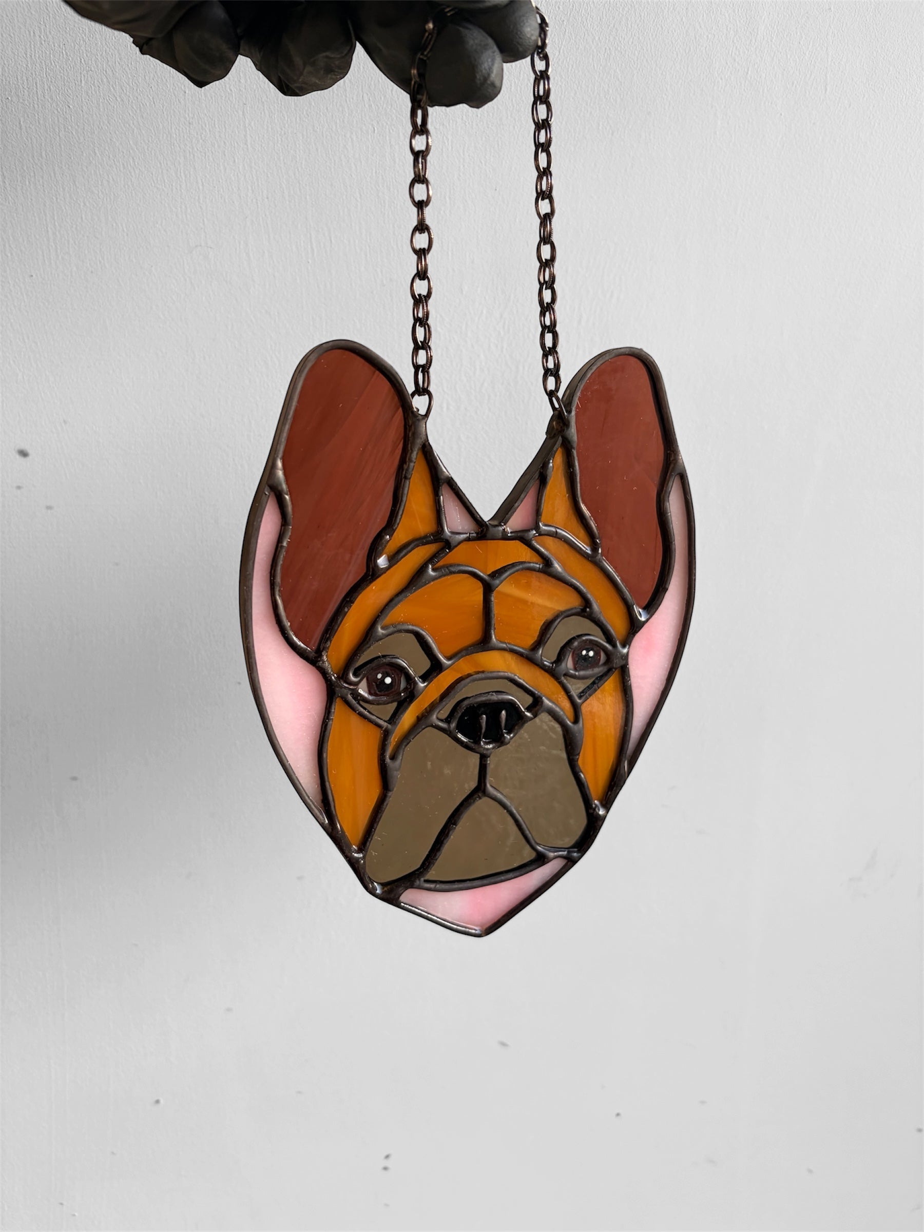 Stained glass pendant of a dog's face on a chain against a white background