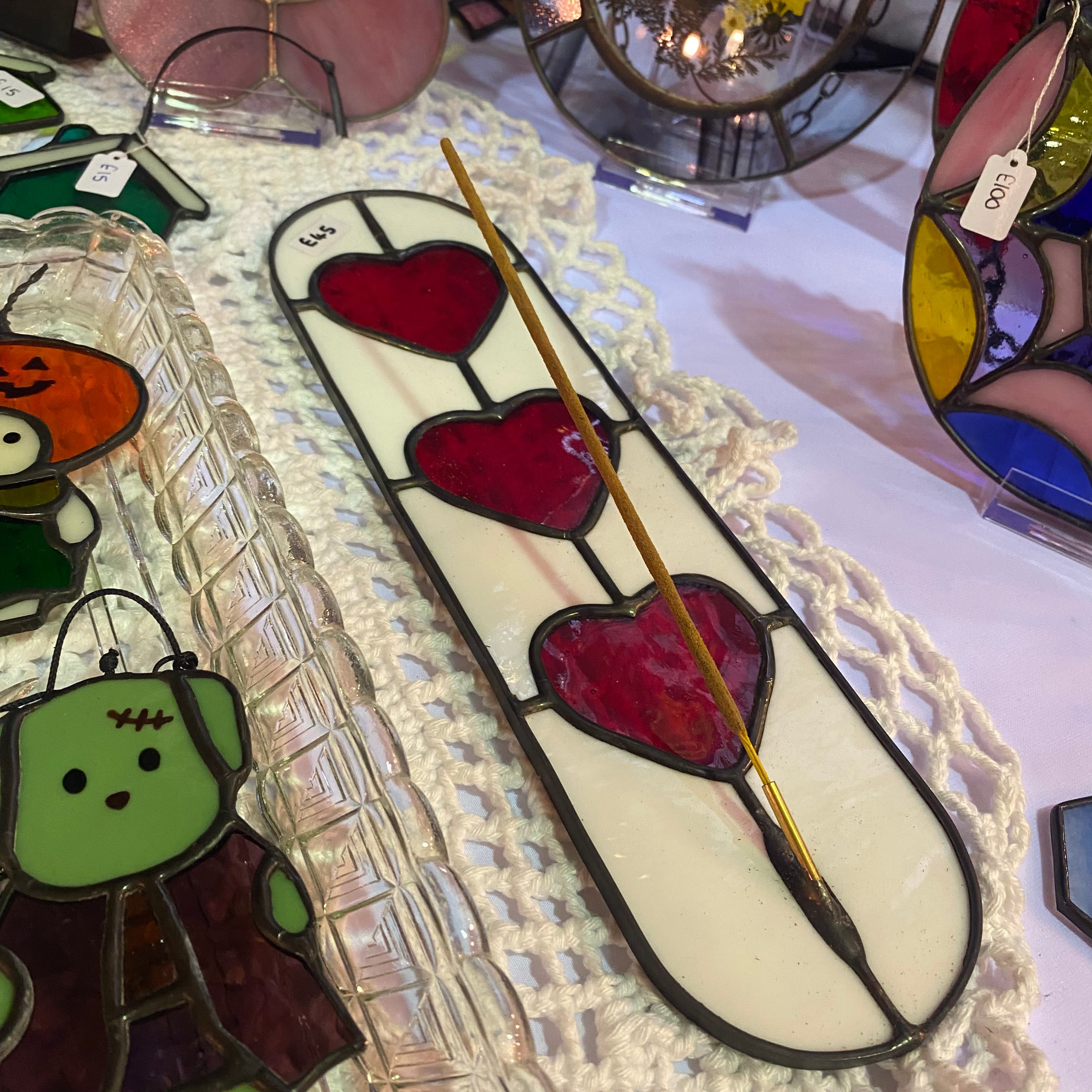 Stained glass incense stick holder with hearts like a playing card on a table with other decorative items.