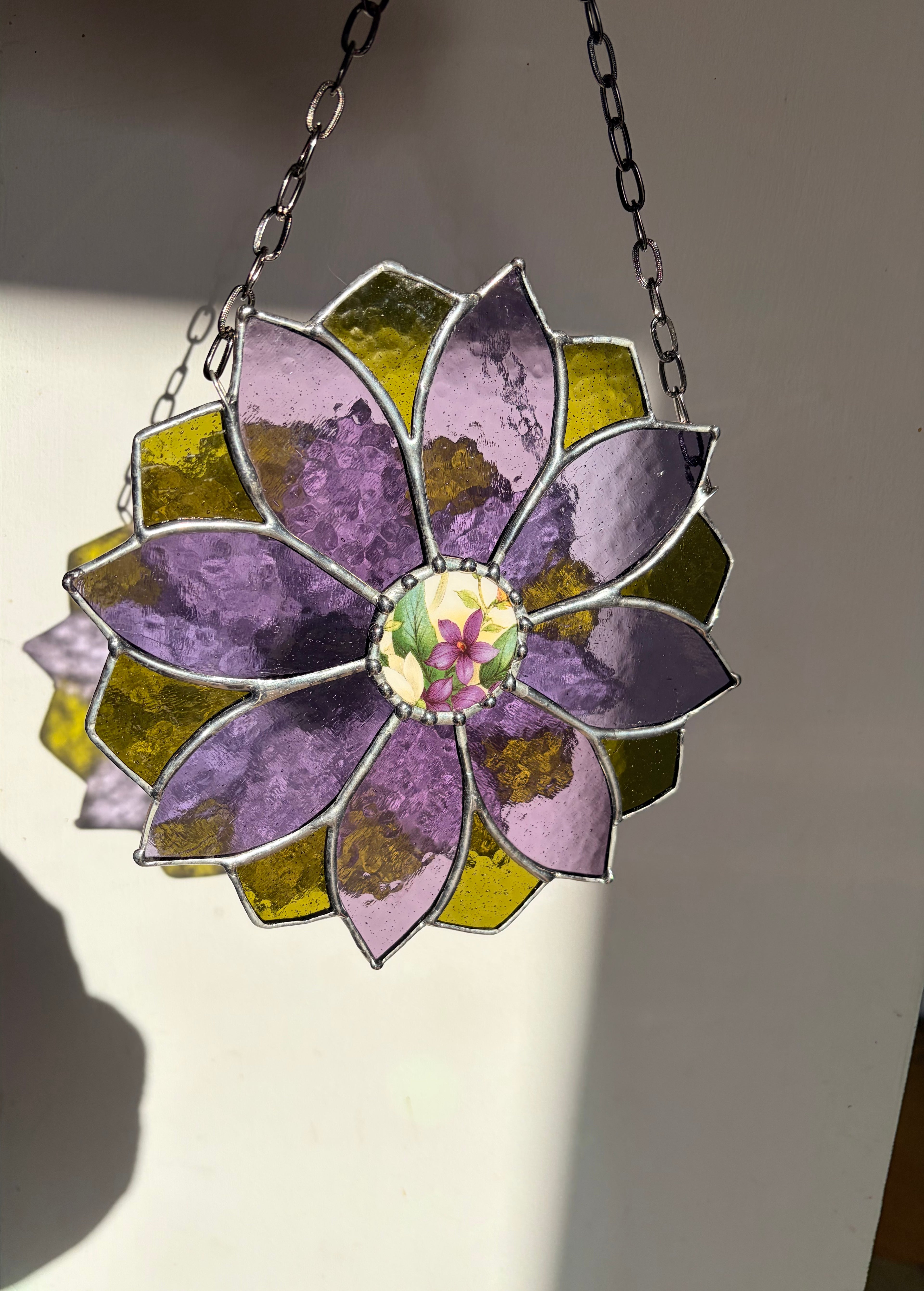 Stained glass flower hanging on a chain against a neutral background