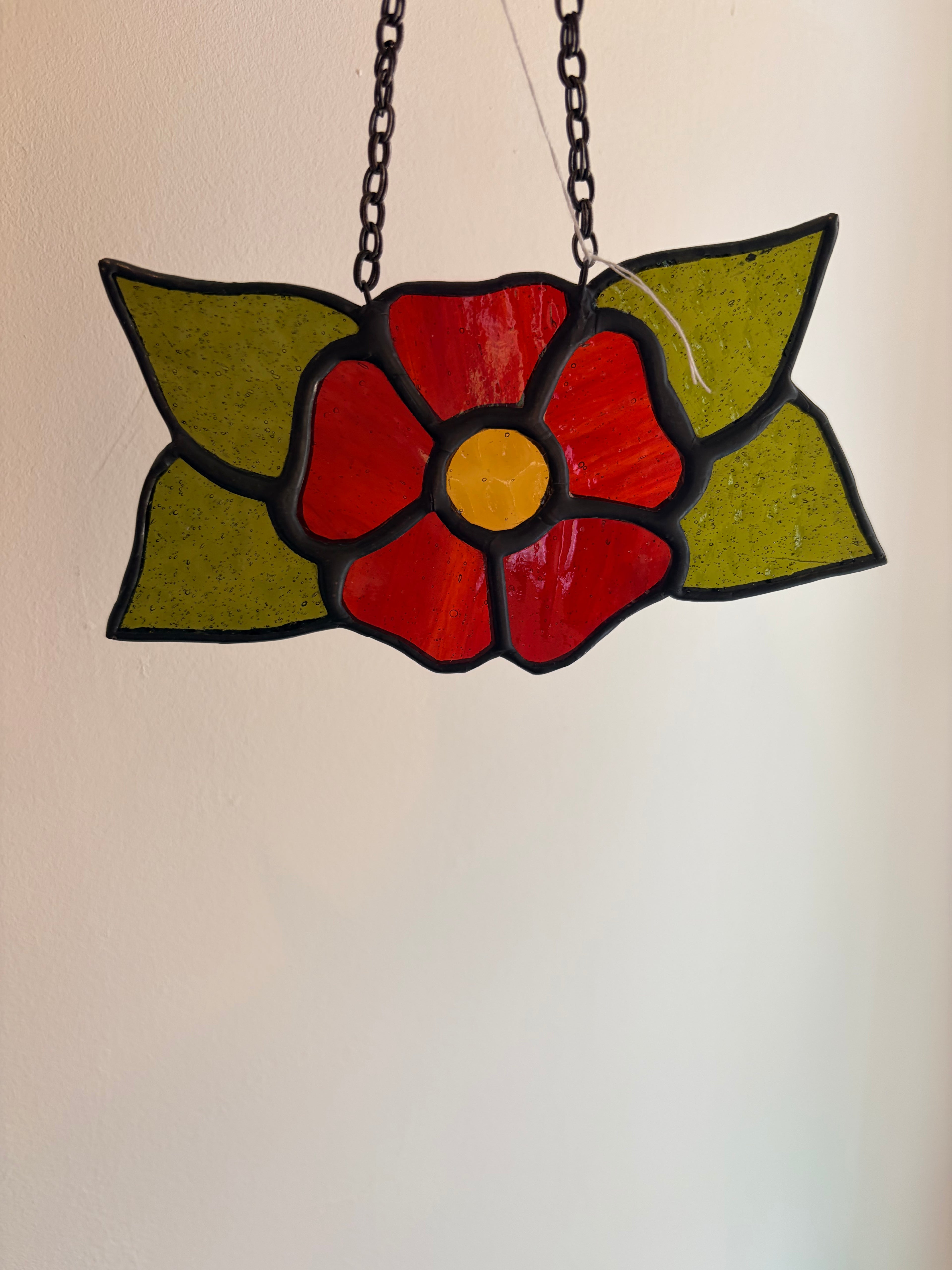 Stained glass flower pendant with red center and green leaves on a beige background