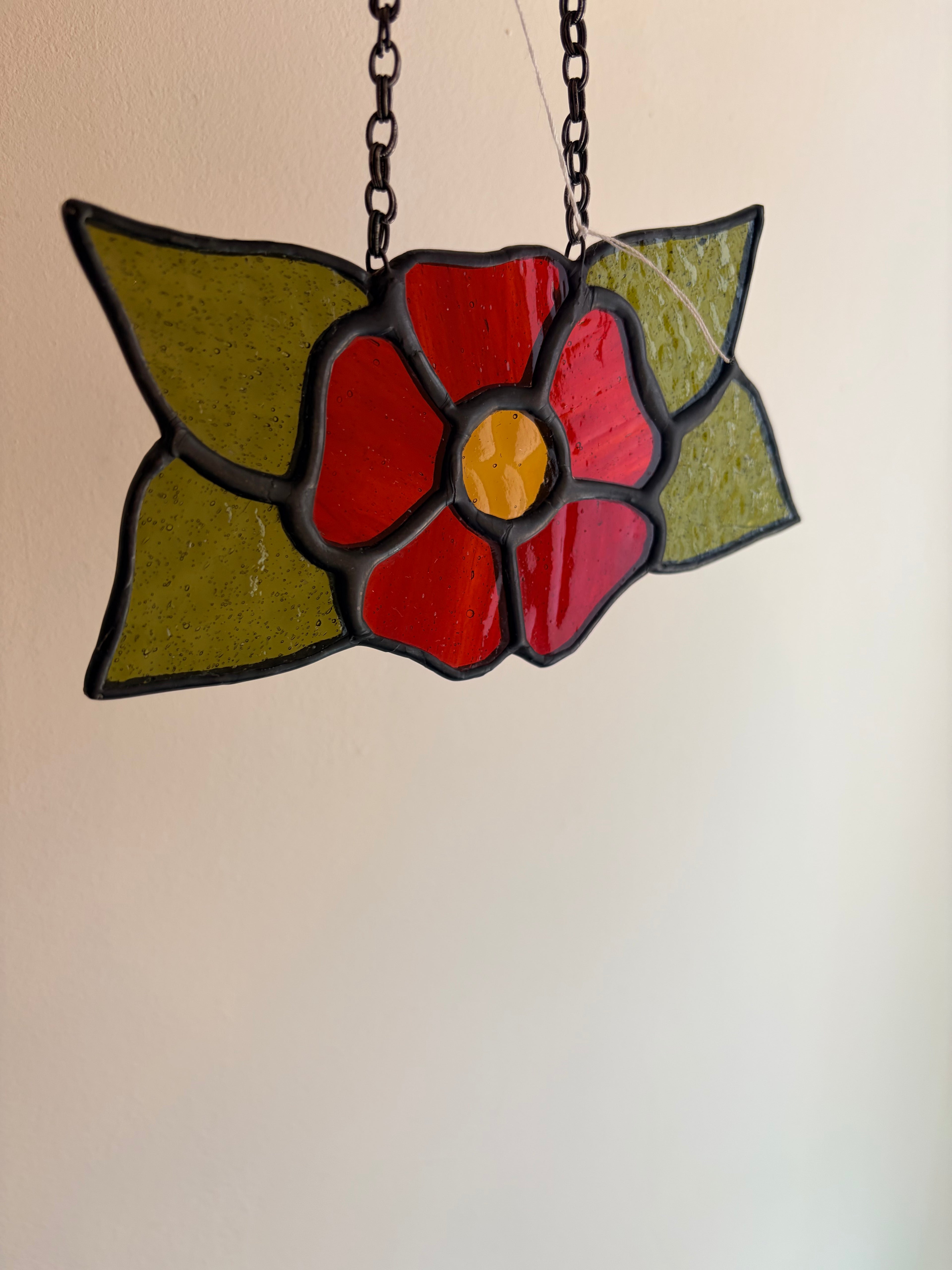 Stained glass flower pendant on a chain against a beige background