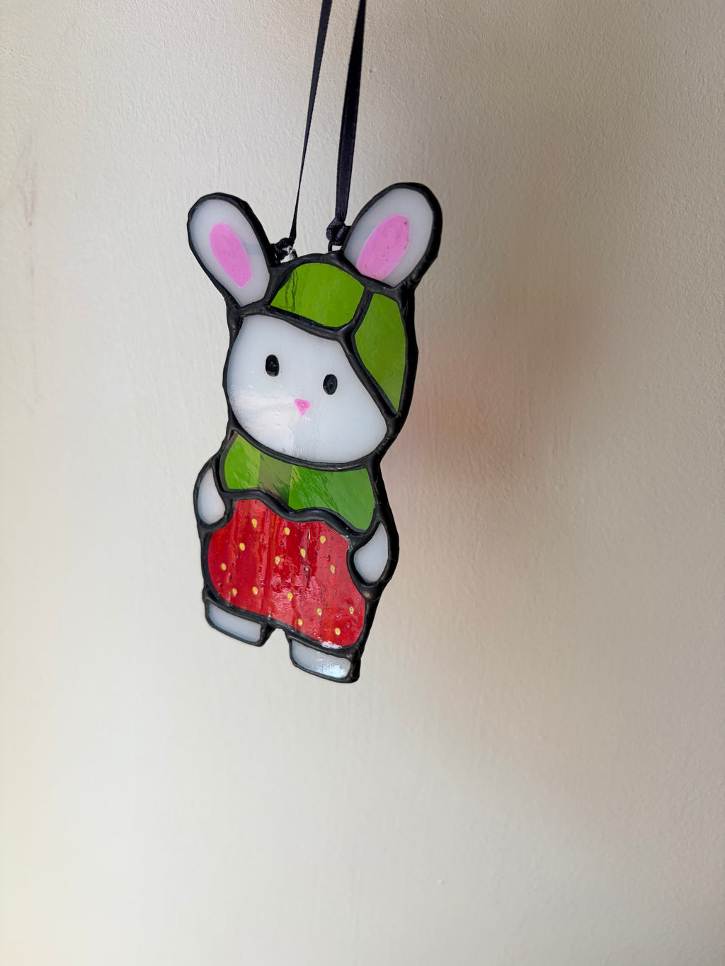 Stained glass bunny with green hat and red strawberry on a plain background