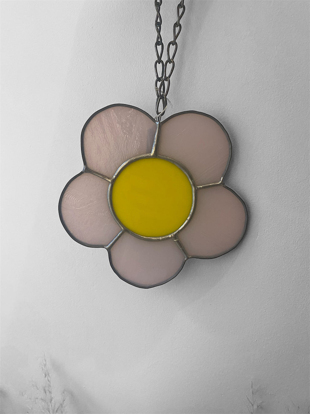 Flower-shaped stained glass suncatcher with yellow centre and pink petals on a chain against a light gray background