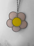 Flower-shaped stained glass suncatcher with yellow centre and pink petals on a chain against a light gray background