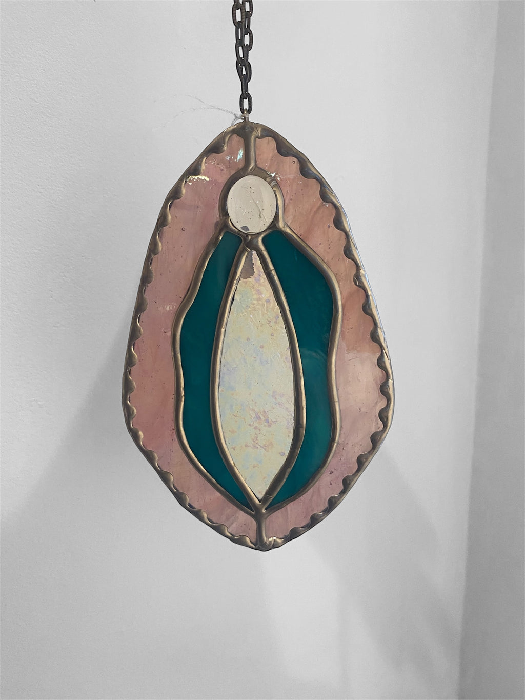 Stained glass yoni vagina suncatcher with turquoise and iridescent pink design on a plain background
