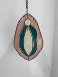 Stained glass yoni vagina suncatcher with turquoise and iridescent pink design on a plain background