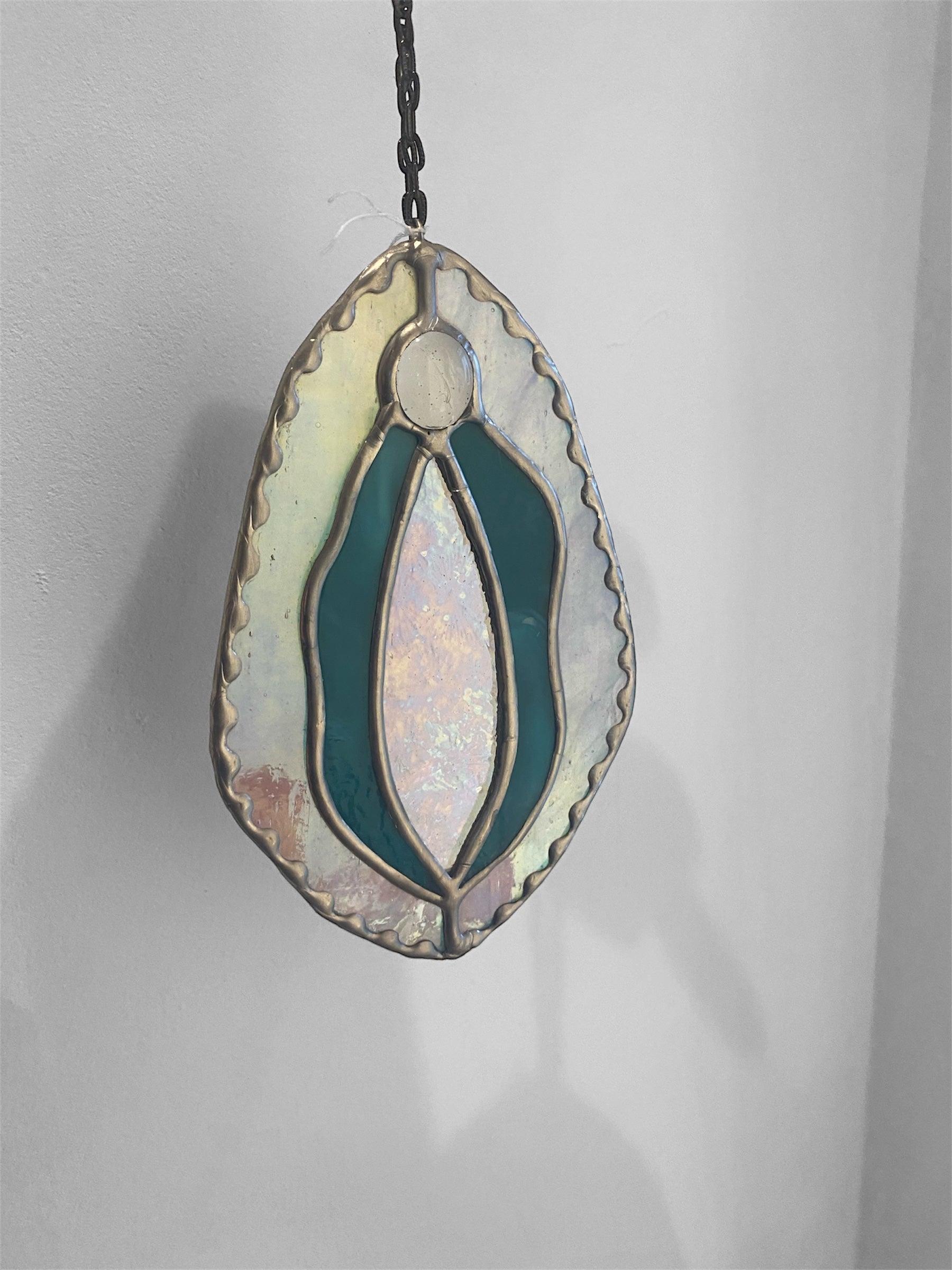 Stained glass yoni vagina suncatcher with turquoise and iridescent pink design on a plain background