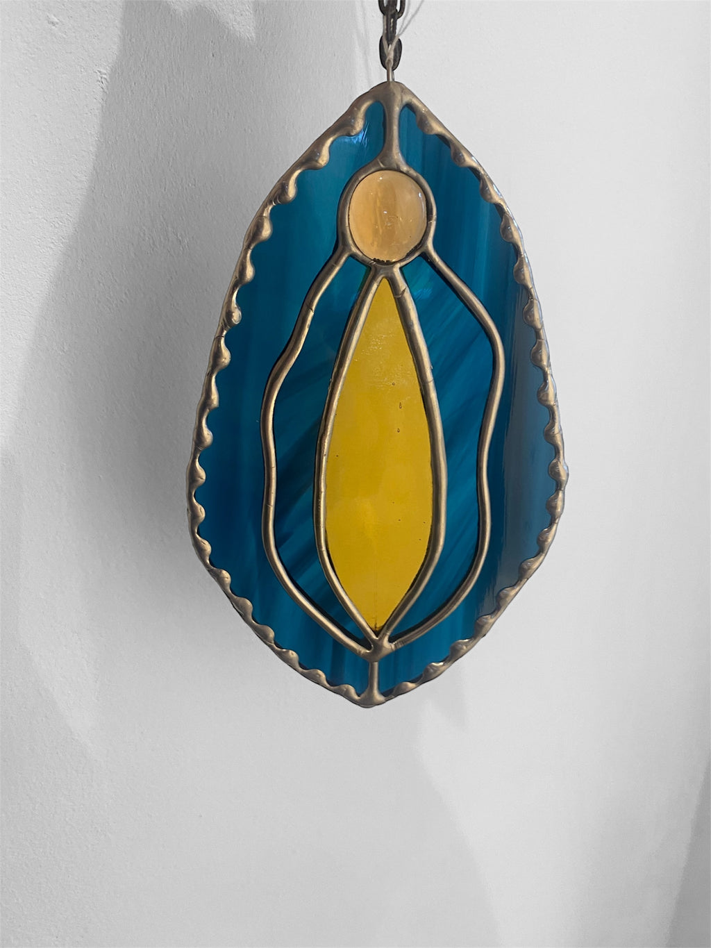 Stained glass yoni vagina suncatcher with dark blue and amber design on a plain background