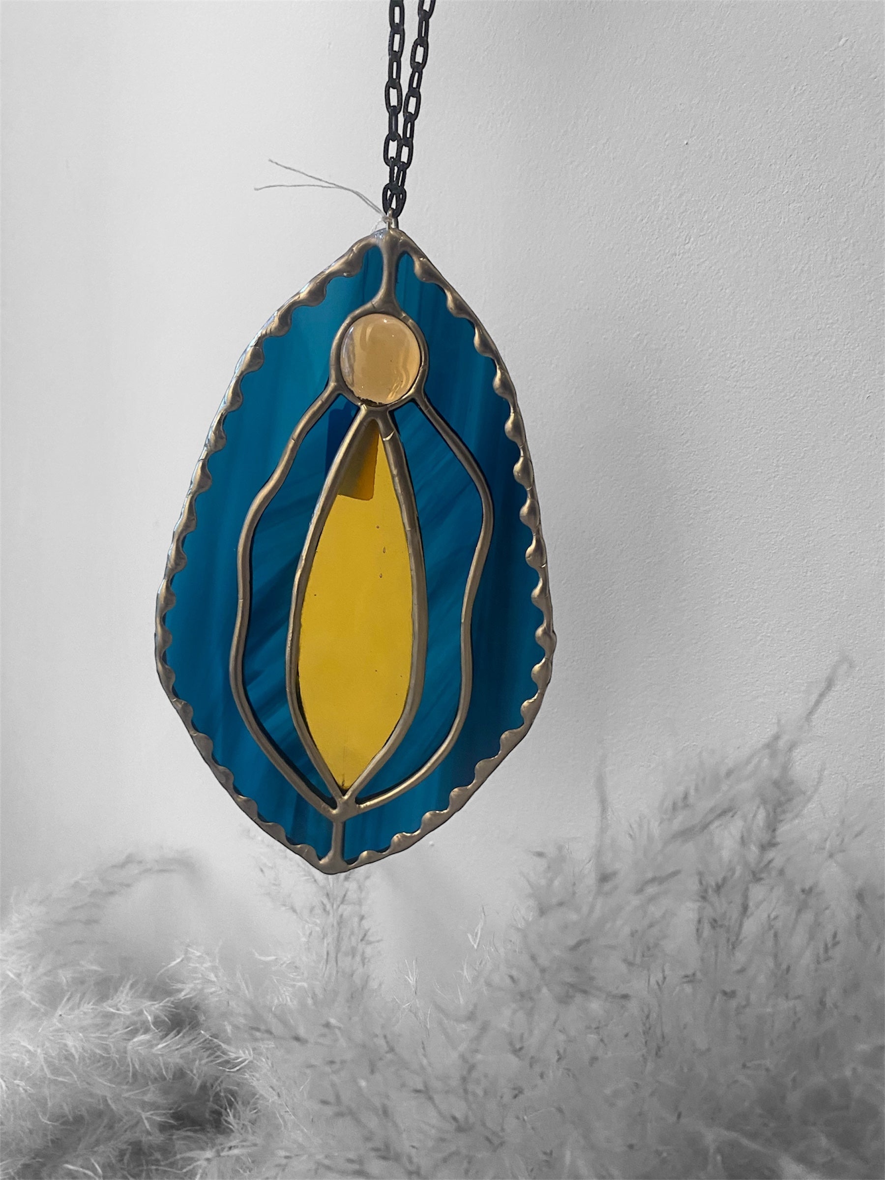 Stained glass yoni vagina suncatcher with dark blue and amber design on a plain background