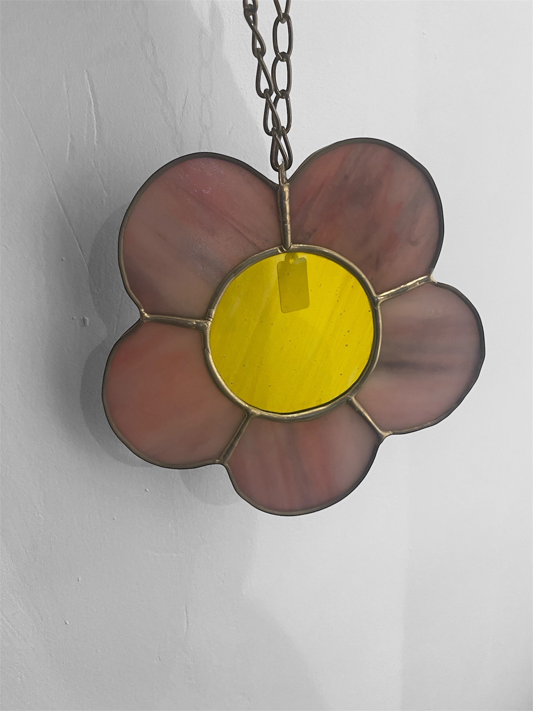 Flower-shaped stained glass suncatcher with yellow center and purple petals on a chain against a gray background