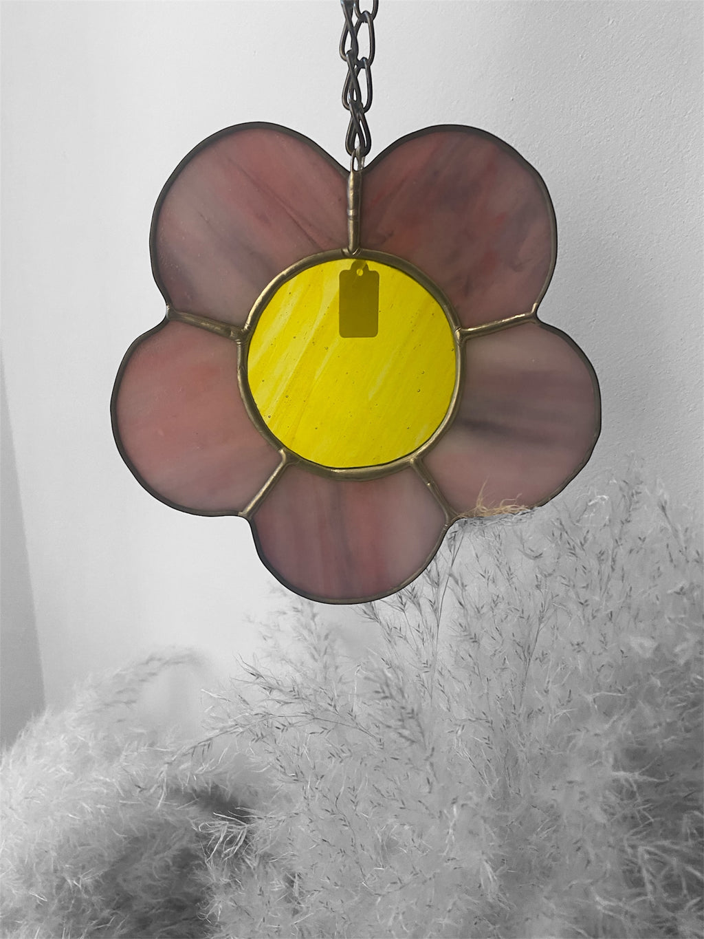 Stained glass flower-shaped ornament with a yellow centre and pink and purple petals on a white background