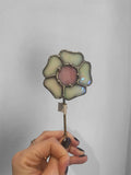 Hand holding a stained glass flower against a plain background