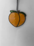 Peach shaped stained glass suncatcher with a yellow center and green leaves on a white background