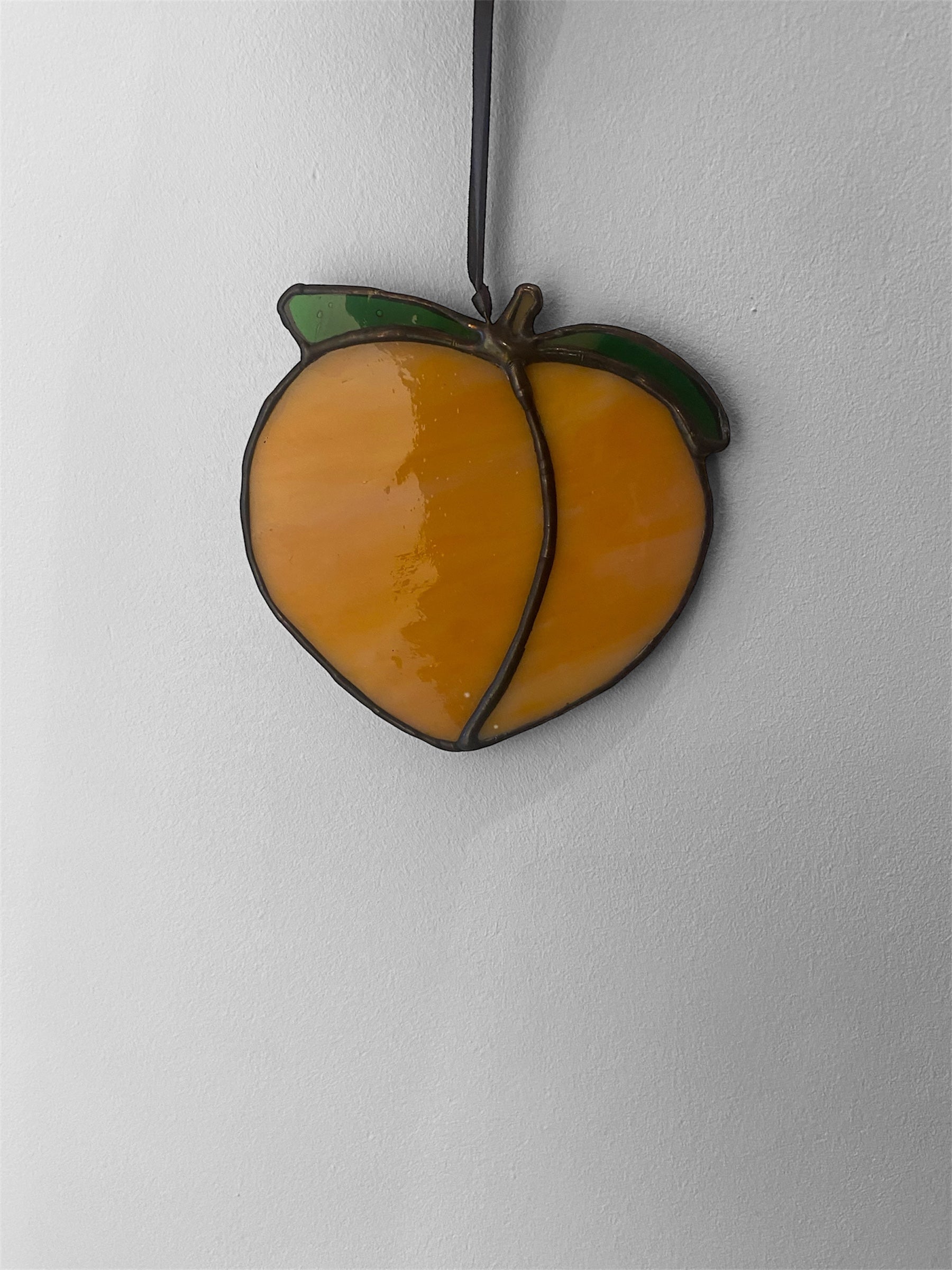 Peach shaped stained glass suncatcher with a yellow center and green leaves on a white background
