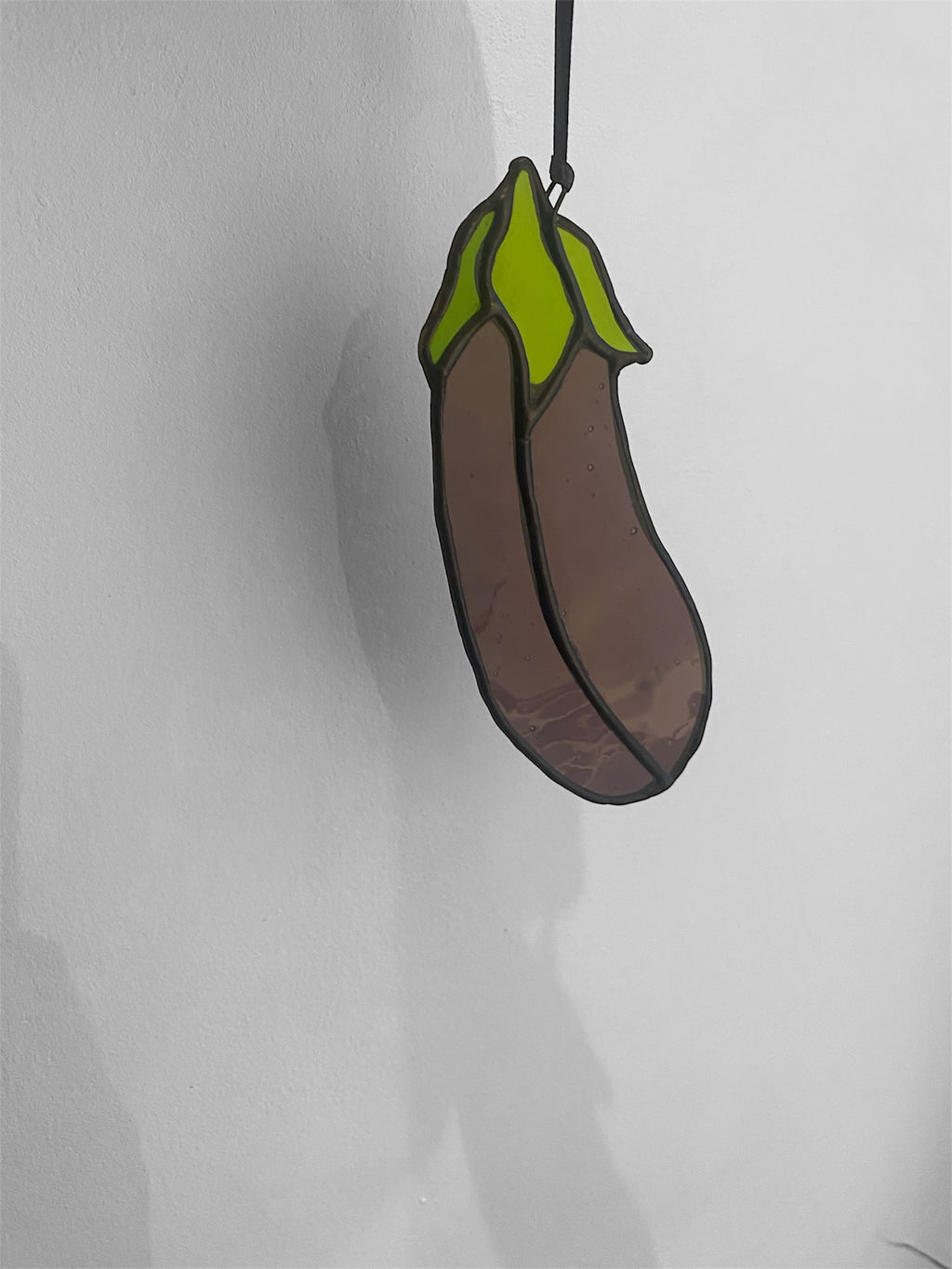 Stained glass suncatcher shaped like an eggplant or aubergine on a white background