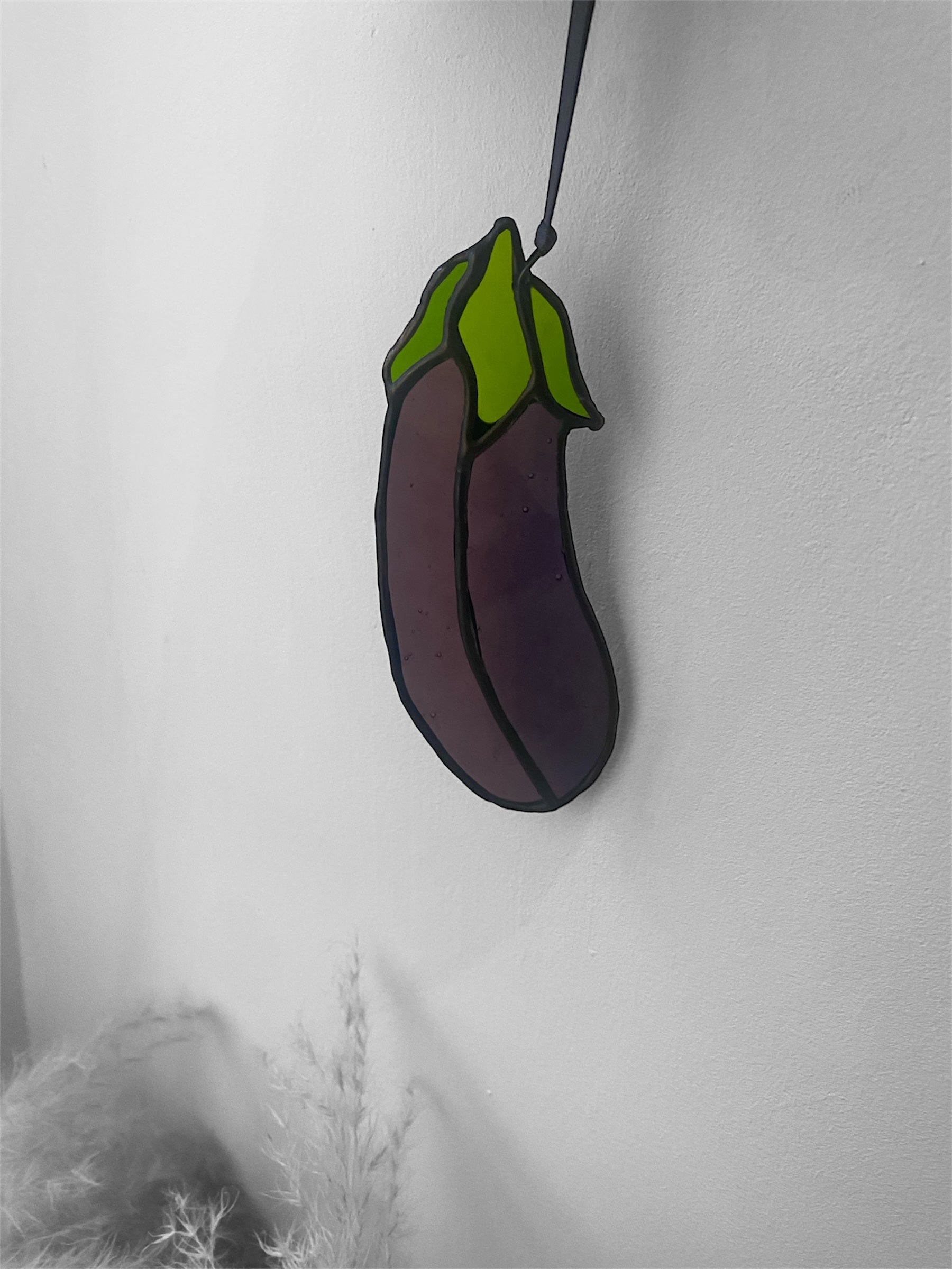 Stained glass suncatcher shaped like an eggplant or aubergine on a white background