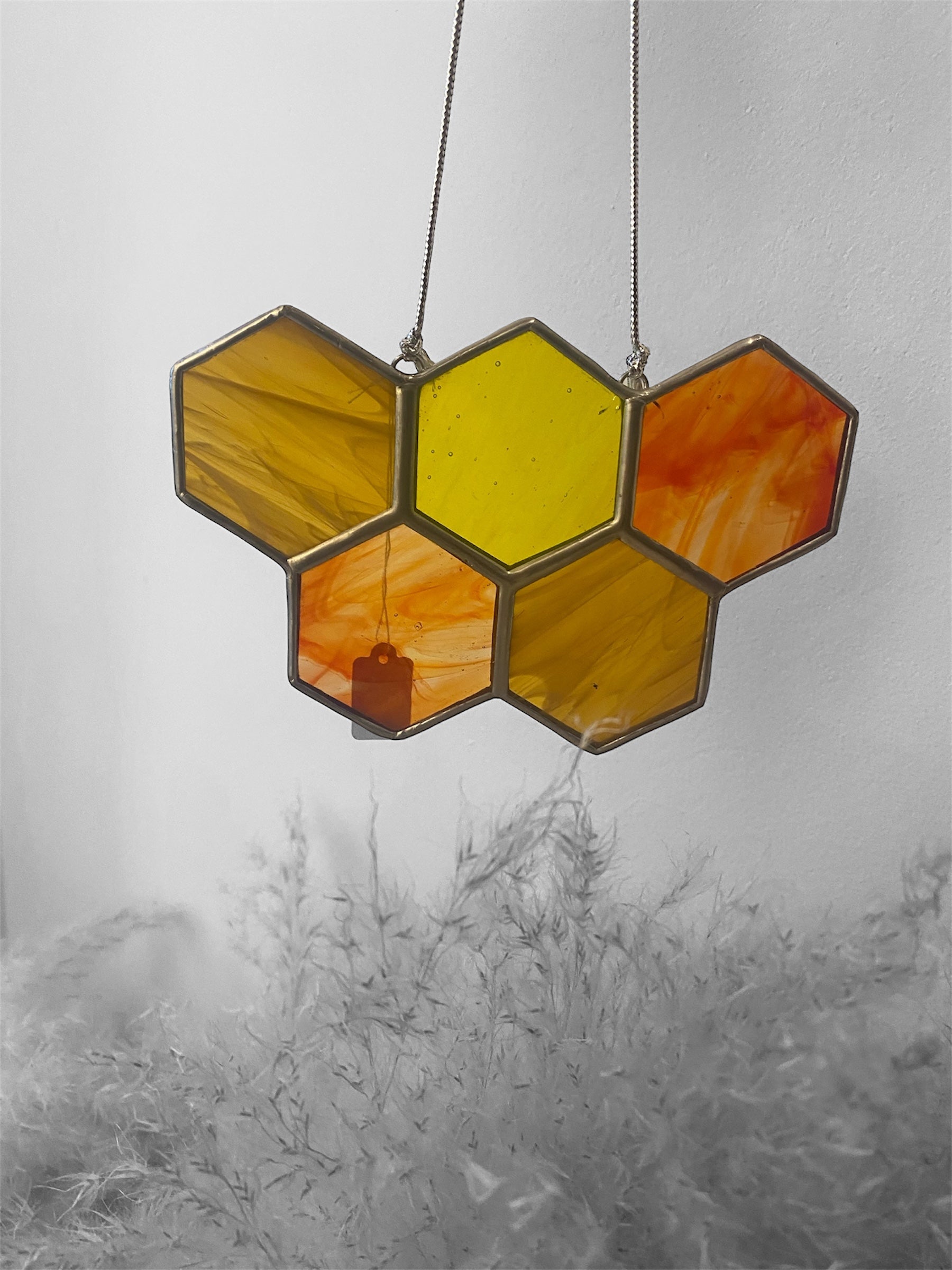 Hexagonal stained glass panel with yellow and orange hues hanging against a white wall.