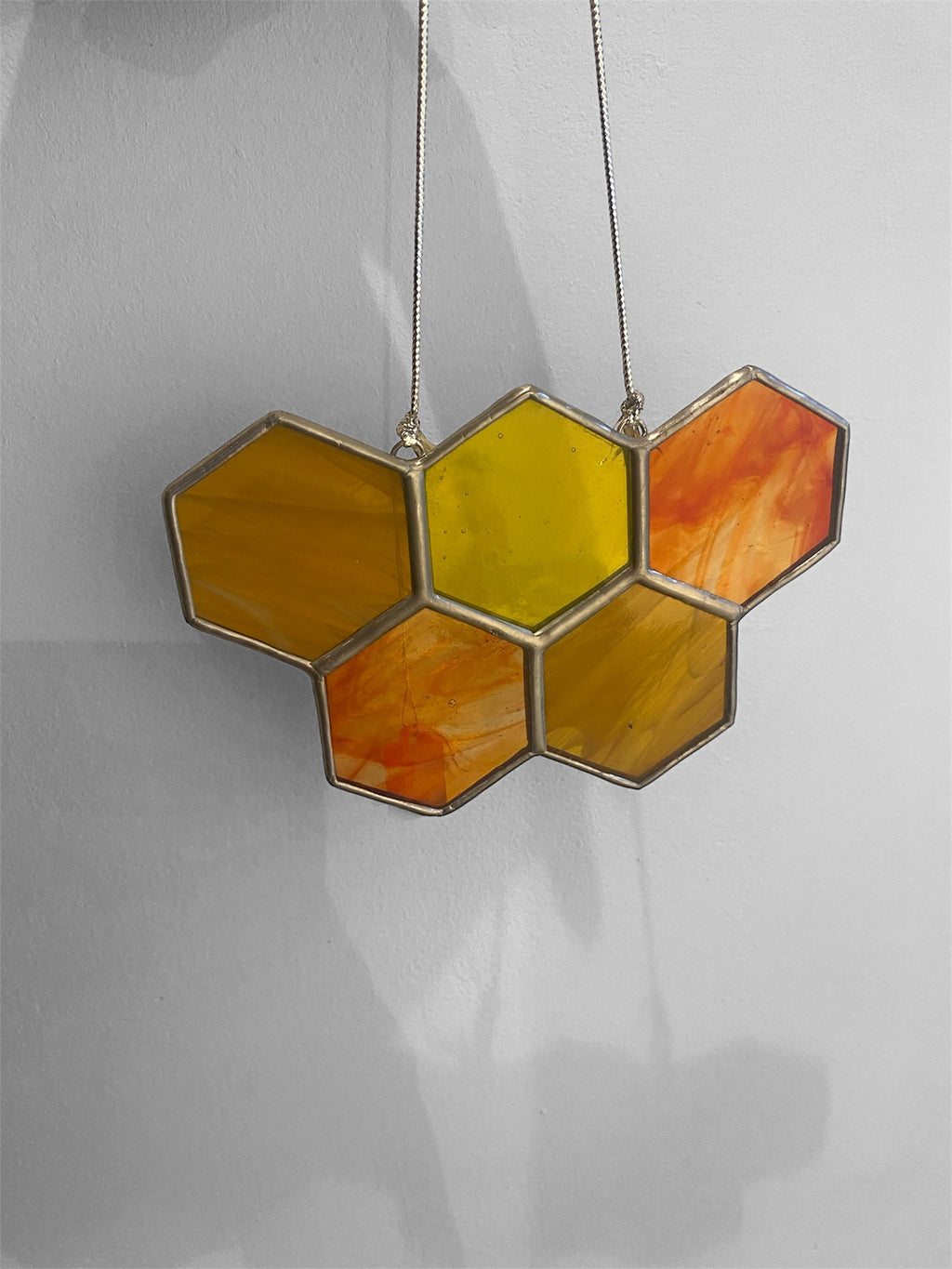 Hexagonal stained glass panel with orange and yellow colors on a plain background