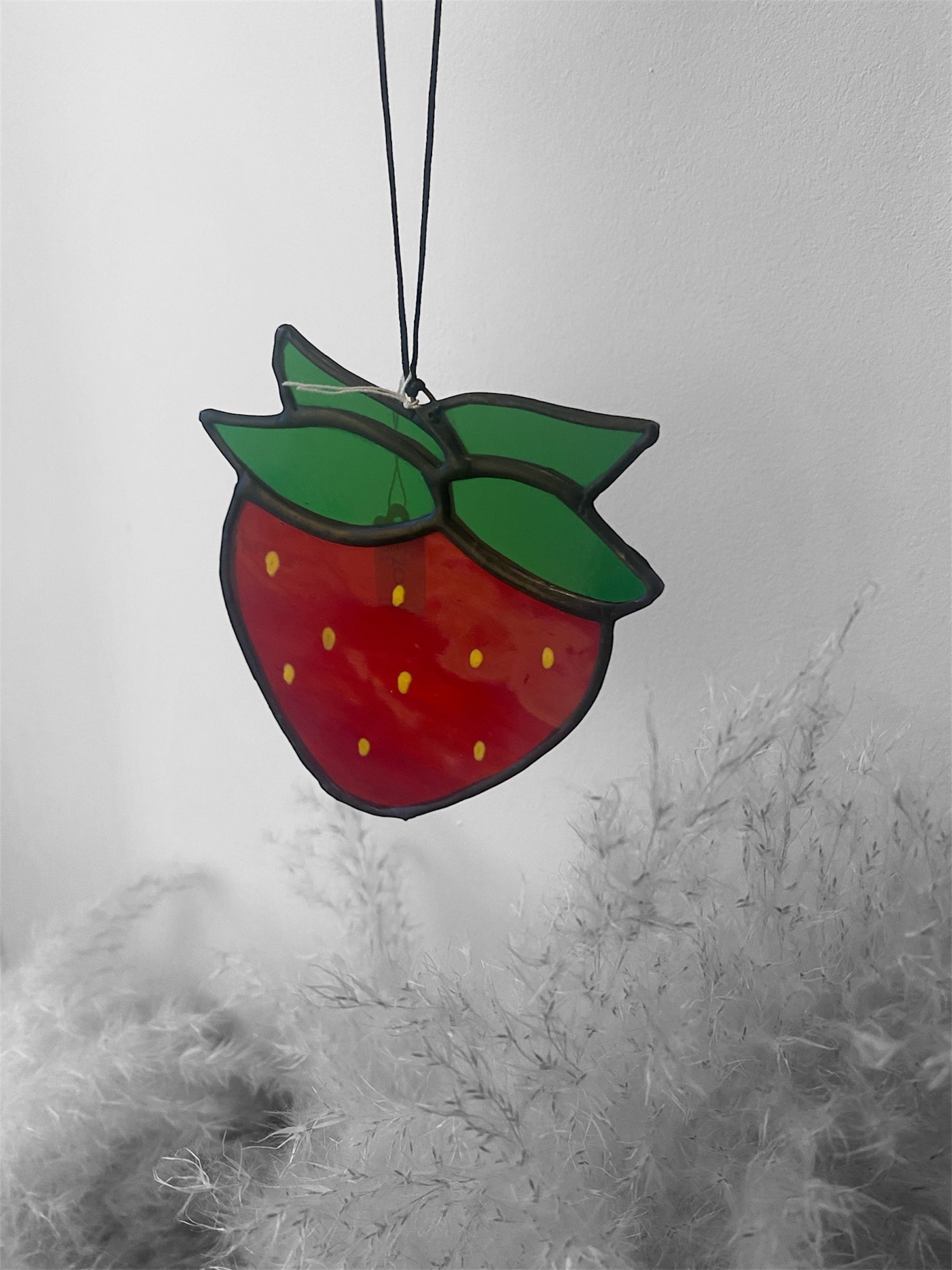 Stained glass strawberry hanging against a snowy window background