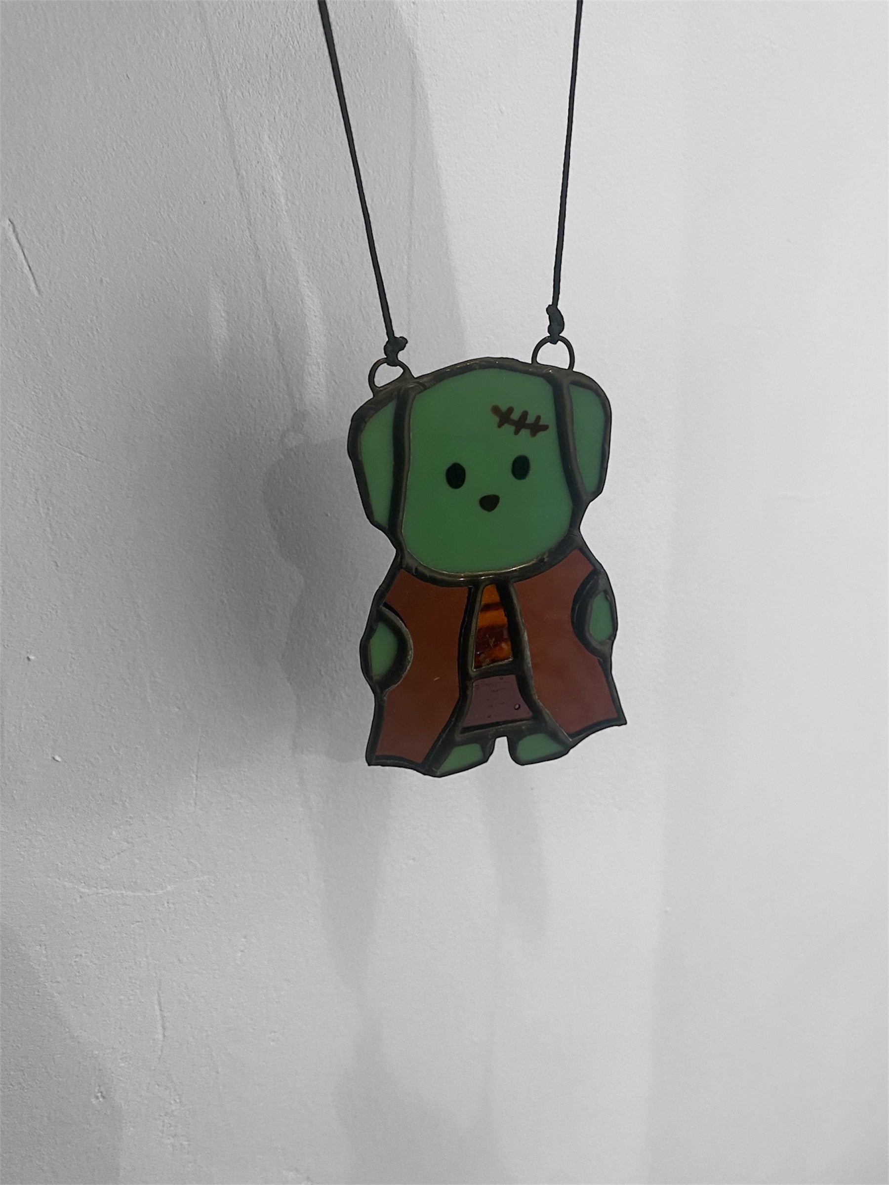 Green zombie dog stained glass ornament on a black cord against a white background