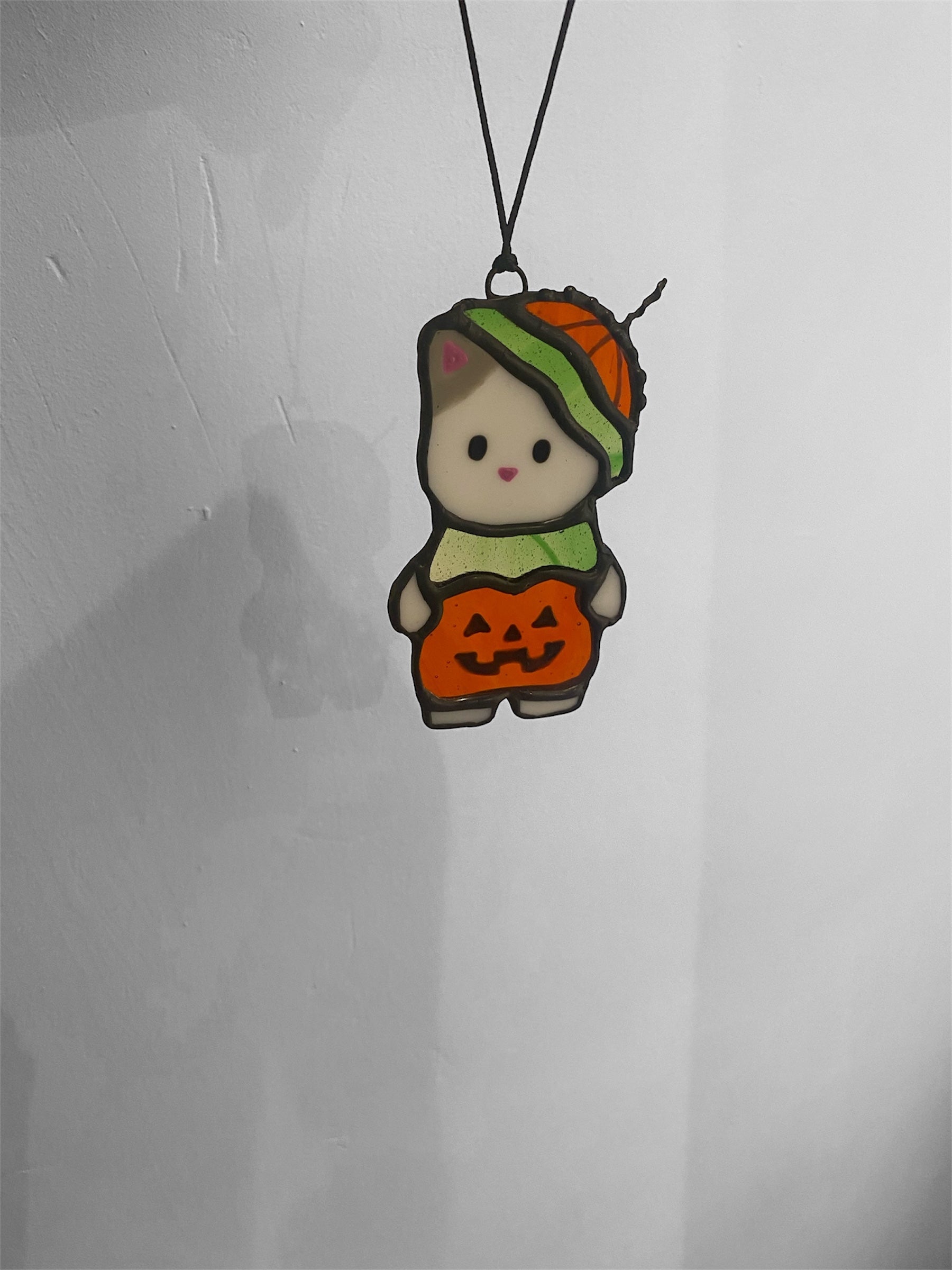 Kawaii-style cat character with a pumpkin stained glass ornament on a gray background