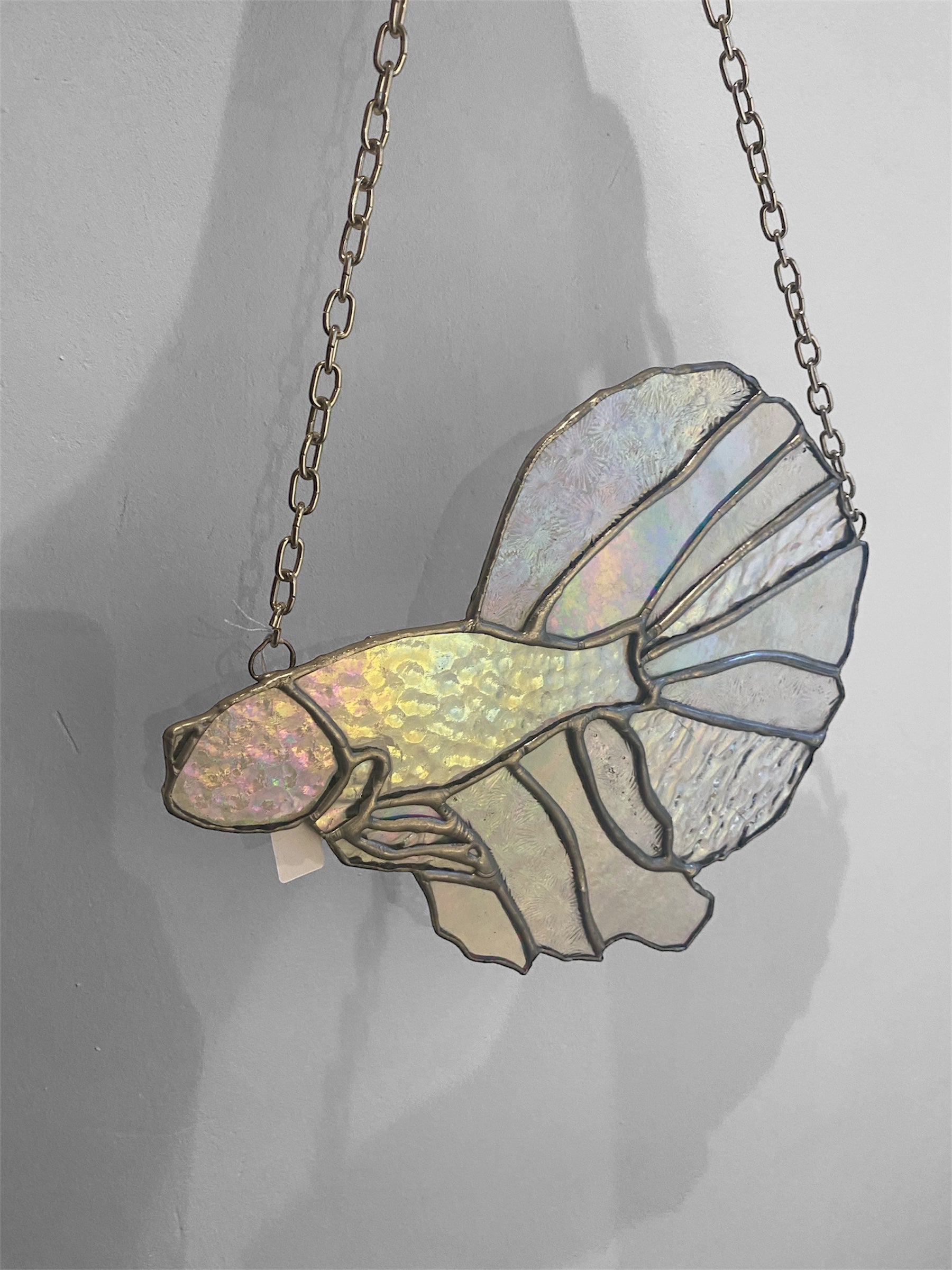 Stained glass fish suncatcher on a chain against a gray background