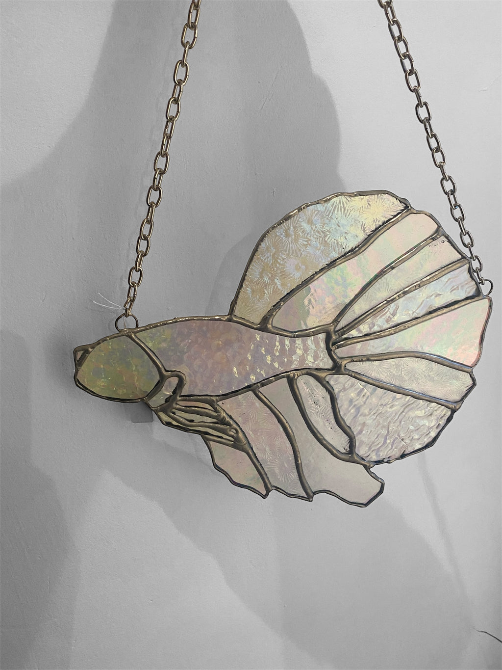 Stained glass fish suncatcher on a chain against a plain background