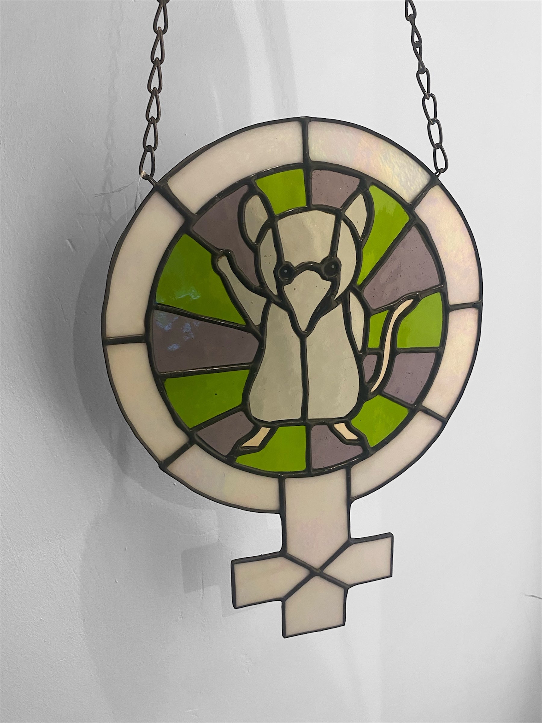 Stained glass window with a design of a shrew and the female symbol on a white background