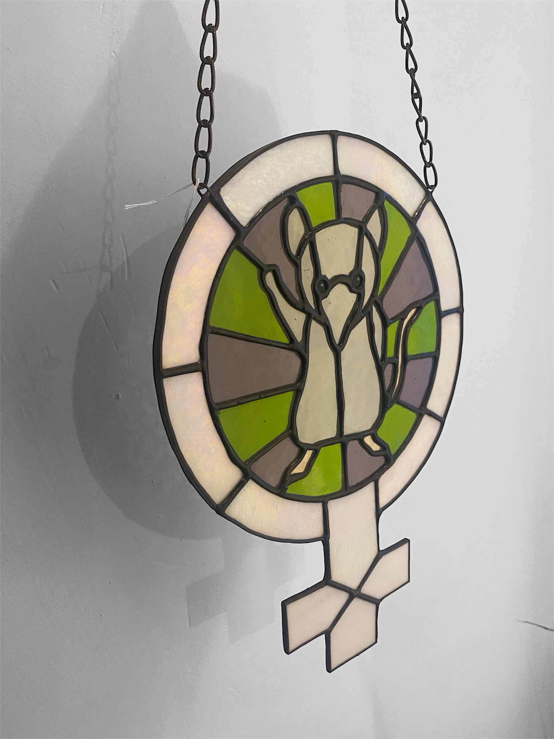 Stained glass window hanging with a shrew pictured within the female symbol.