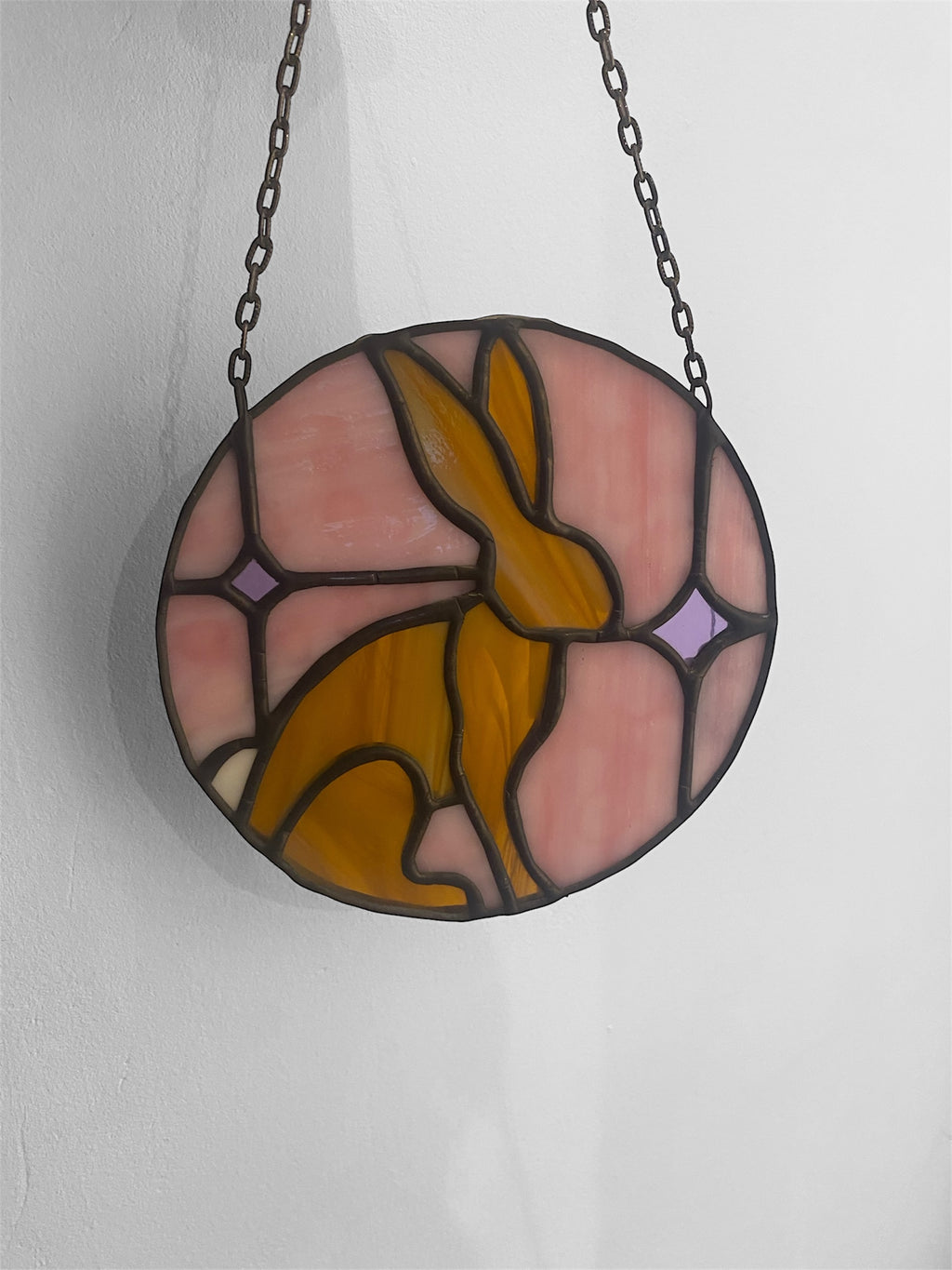 Stained glass window hanging with a rabbit design on a white background