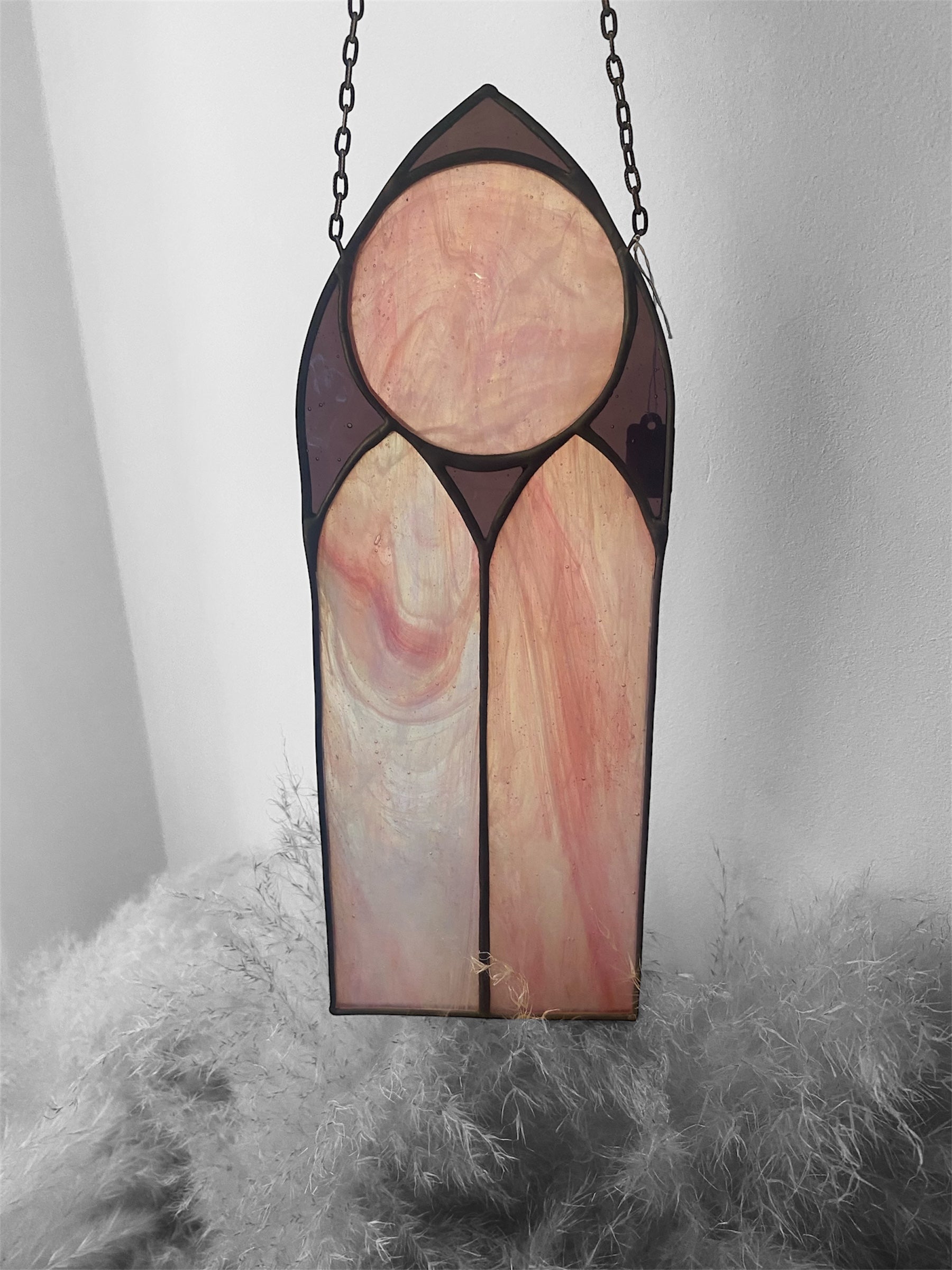 Stained glass panel with pink and purple colors hanging on a chain against a neutral background.