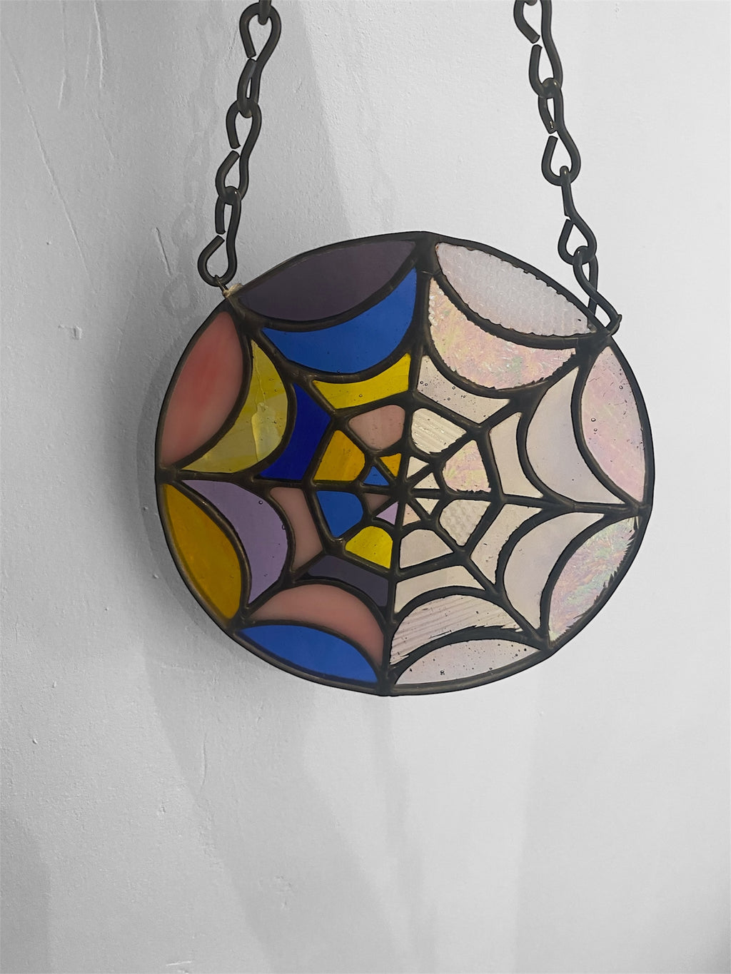 Stained glass spider web design inspired by Wednesday hanging on a chain against a white background