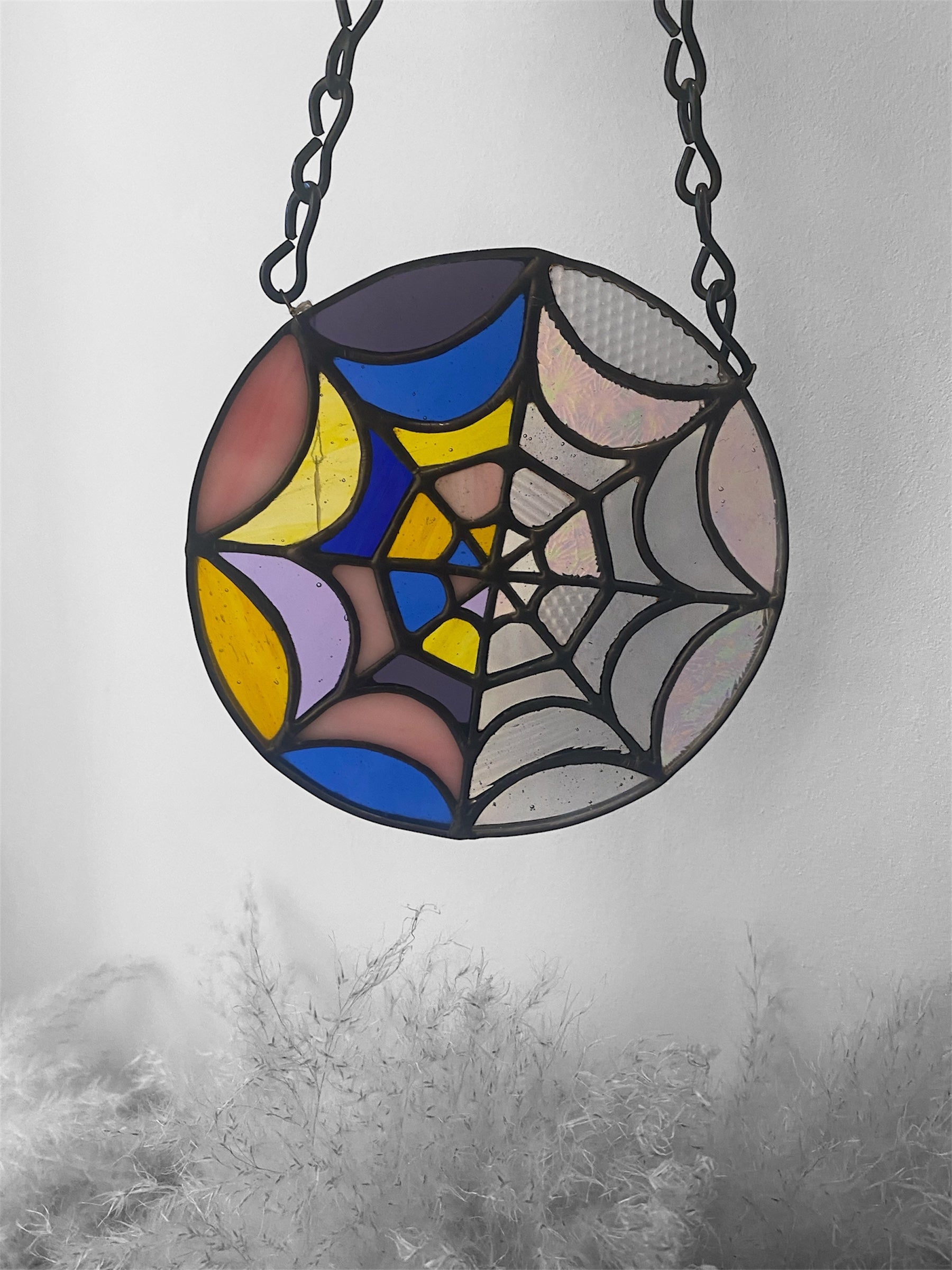 Stained glass spider web design hanging against a gray background