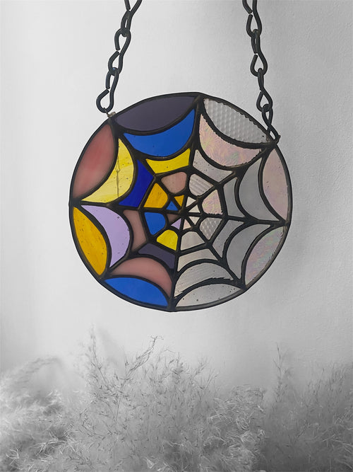 Stained glass spider web design hanging against a gray background