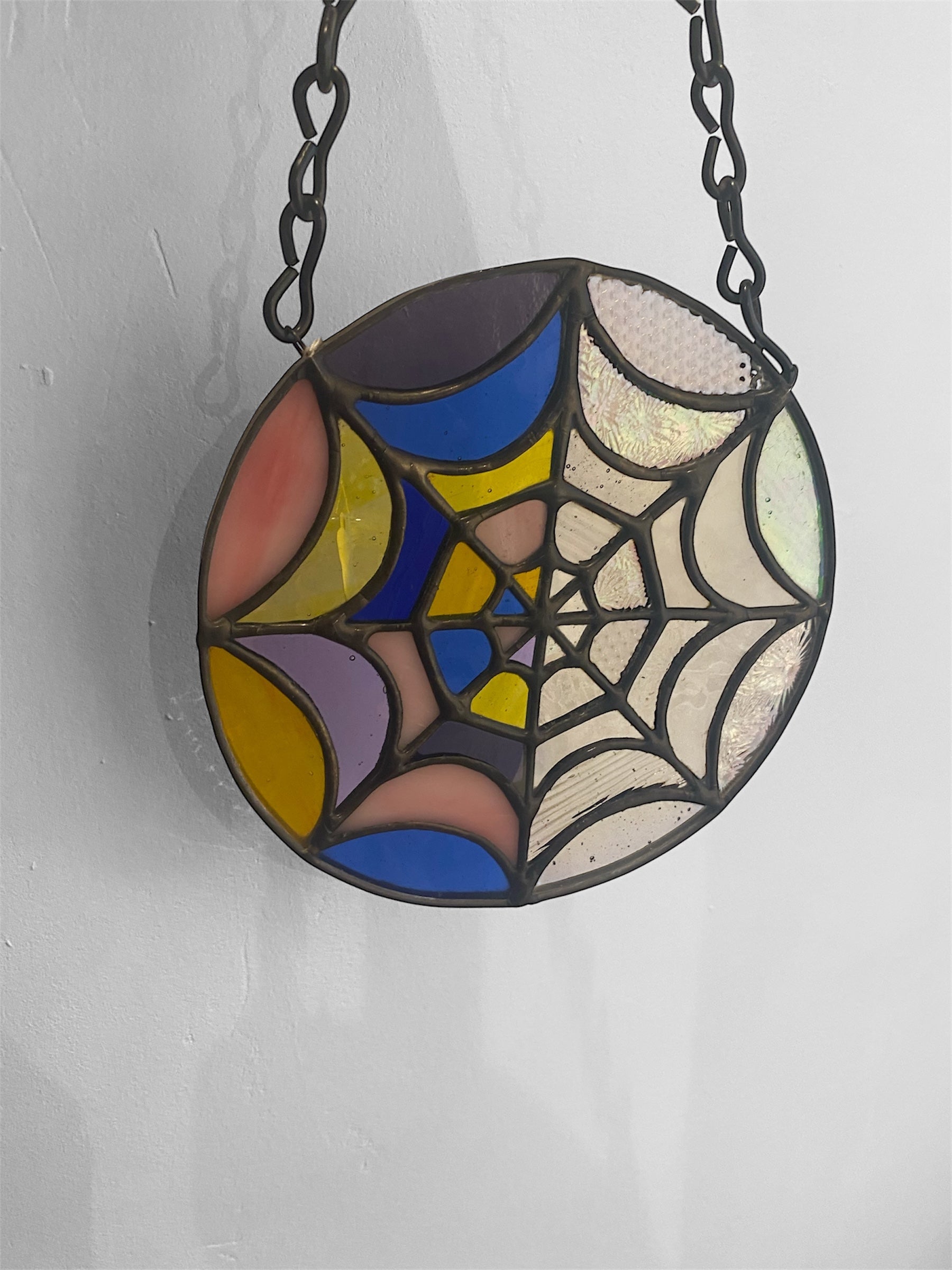 Stained glass suncatcher with spider web design on a chain against a white background
