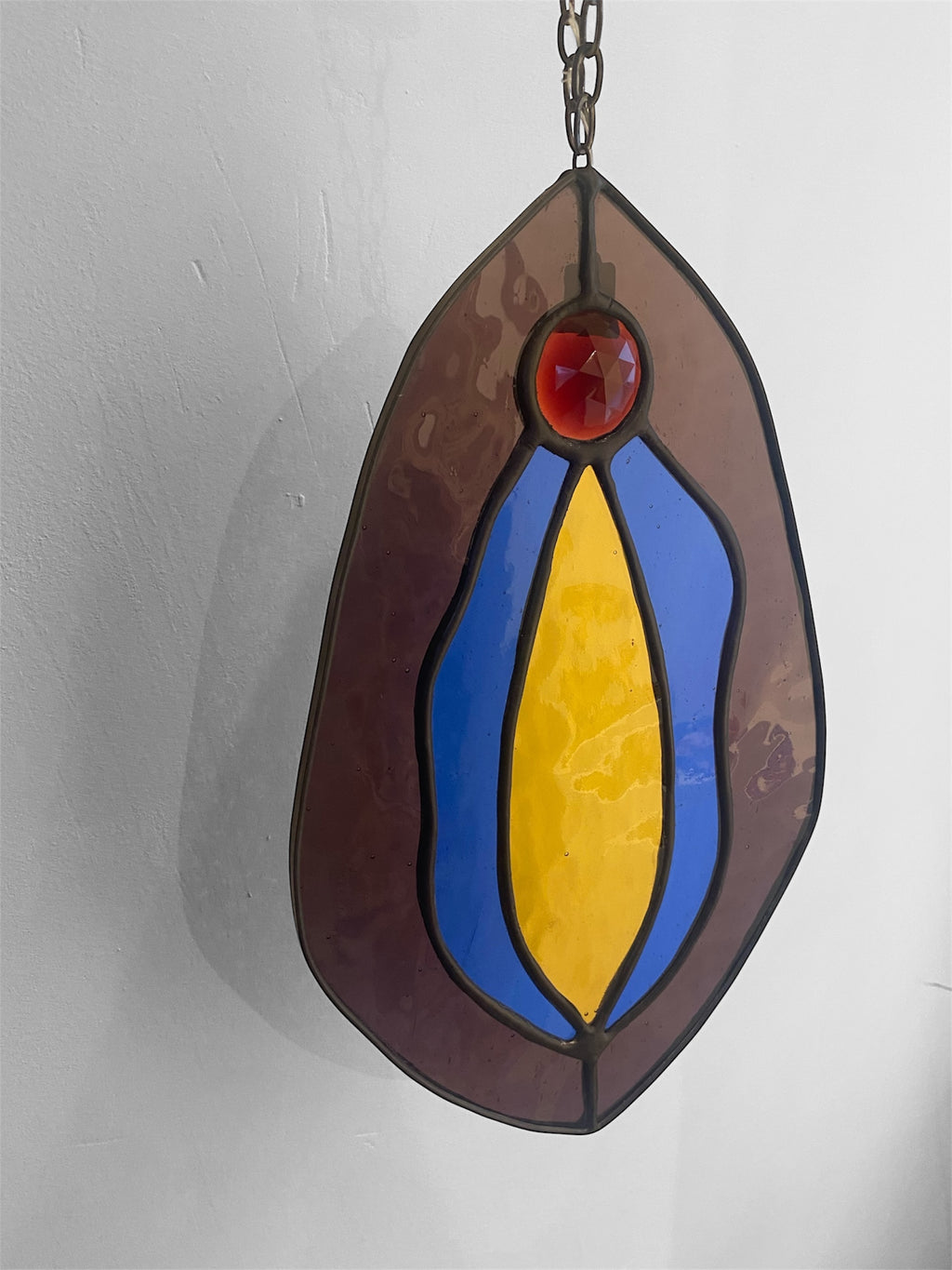 Stained glass hanging panel with red, blue, and yellow colors on a plain background