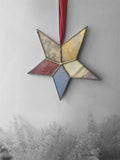 Star-shaped stained glass ornament with a pink ribbon on a textured gray background