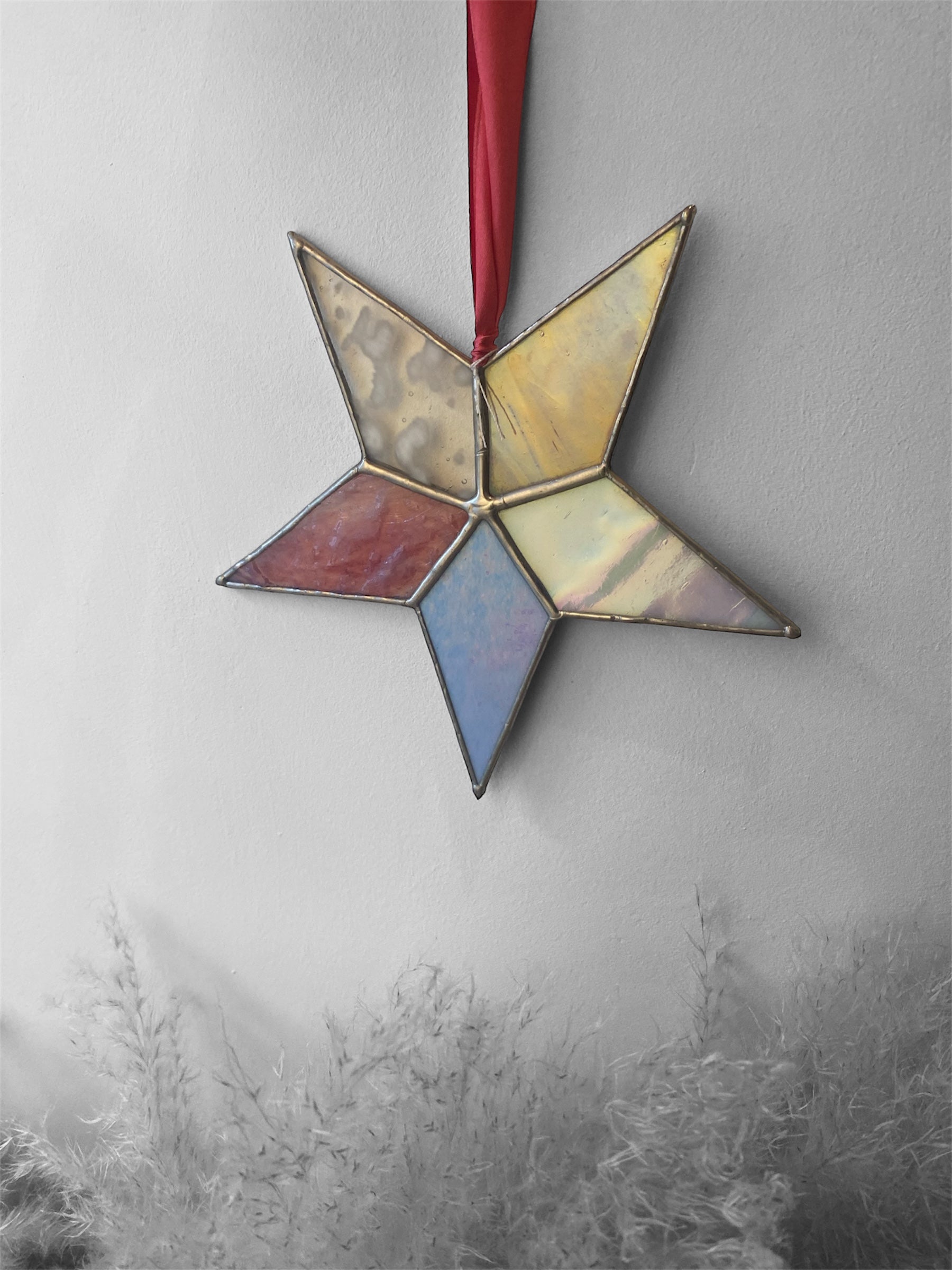 Star-shaped stained glass ornament with a pink ribbon on a textured gray background