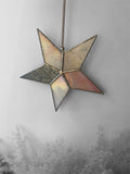 Decorative star-shaped stained glass suncatcher with a textured surface on a gray background