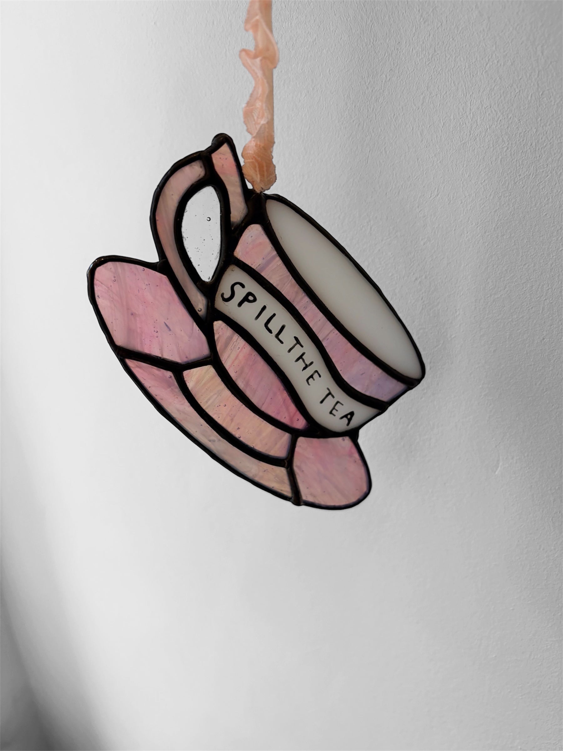 A pink iridescent glass teacup with a funny phrase painted on the side, shown from another angle to show the colour of the glass