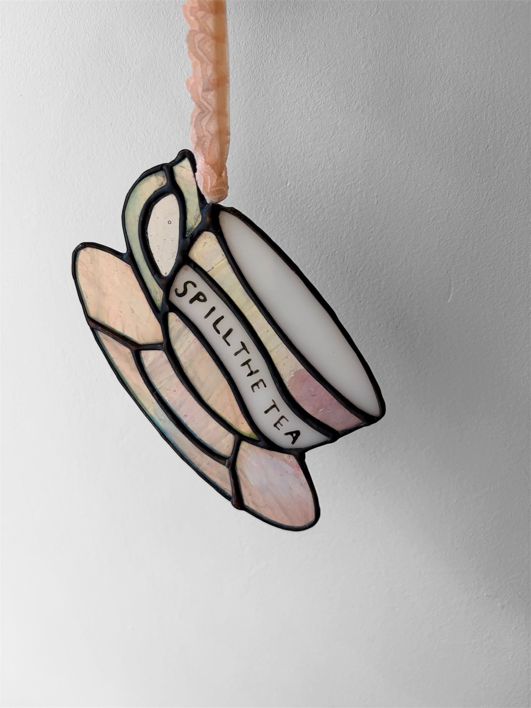 A pink iridescent glass teacup with a funny phrase painted on the side
