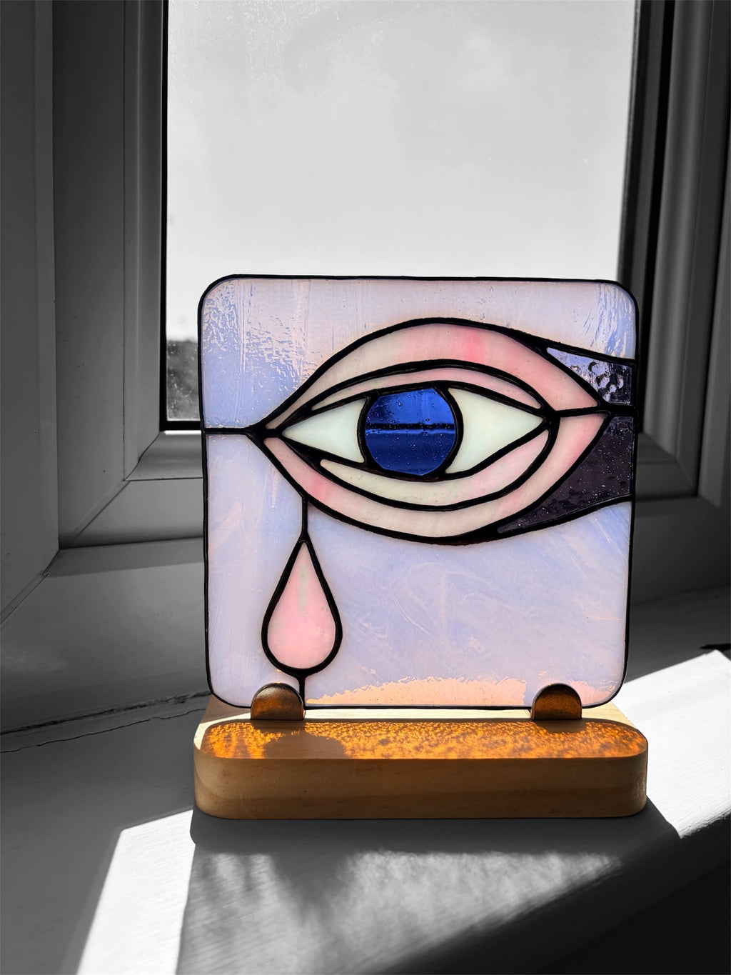 Stained glass art mounted on a wooden stand picturing a pink eye