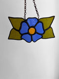 Stained glass flower pendant with blue center and green leaves on a white background
