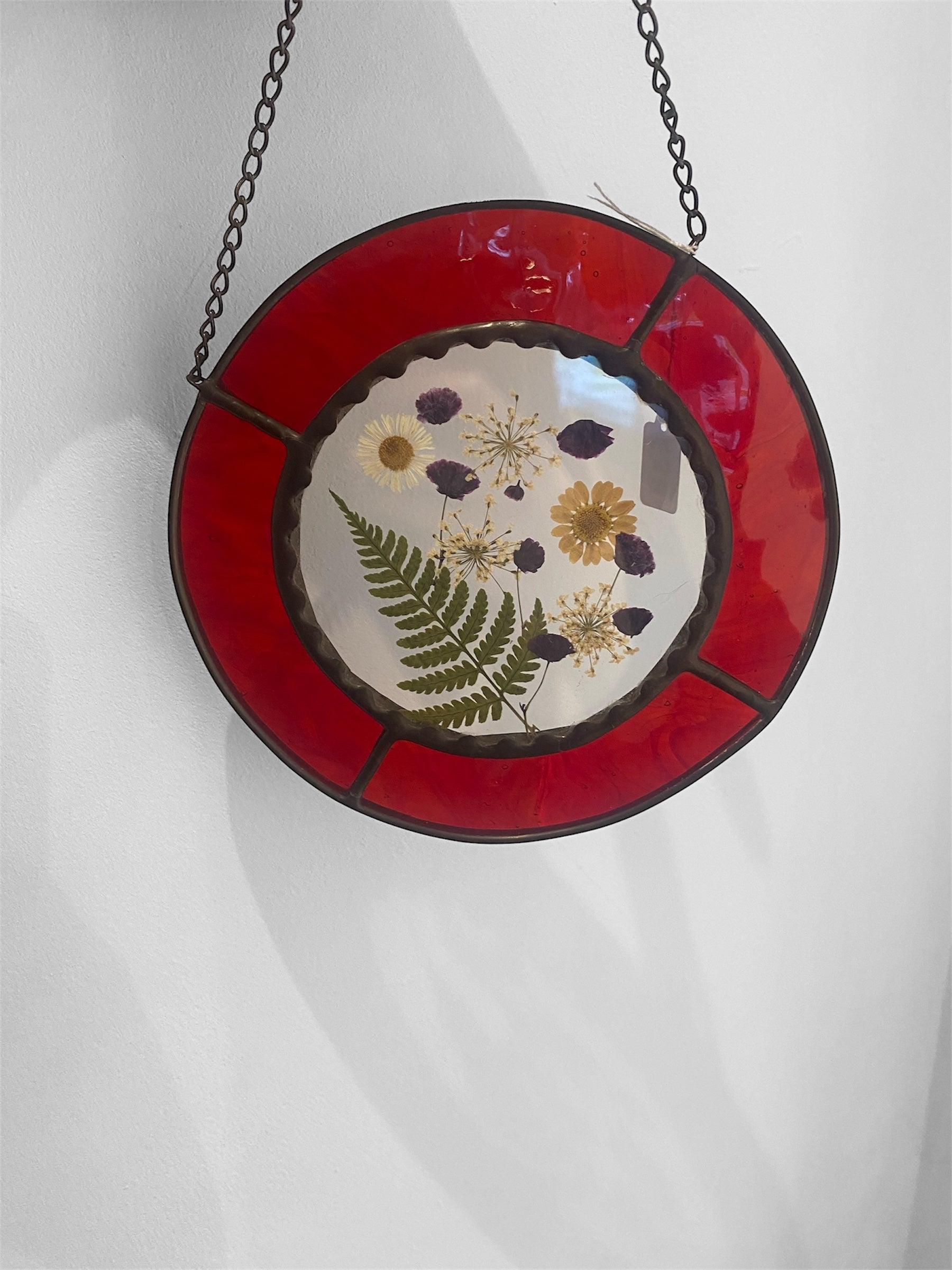 Round stained glass panel with floral design and red border on a white background