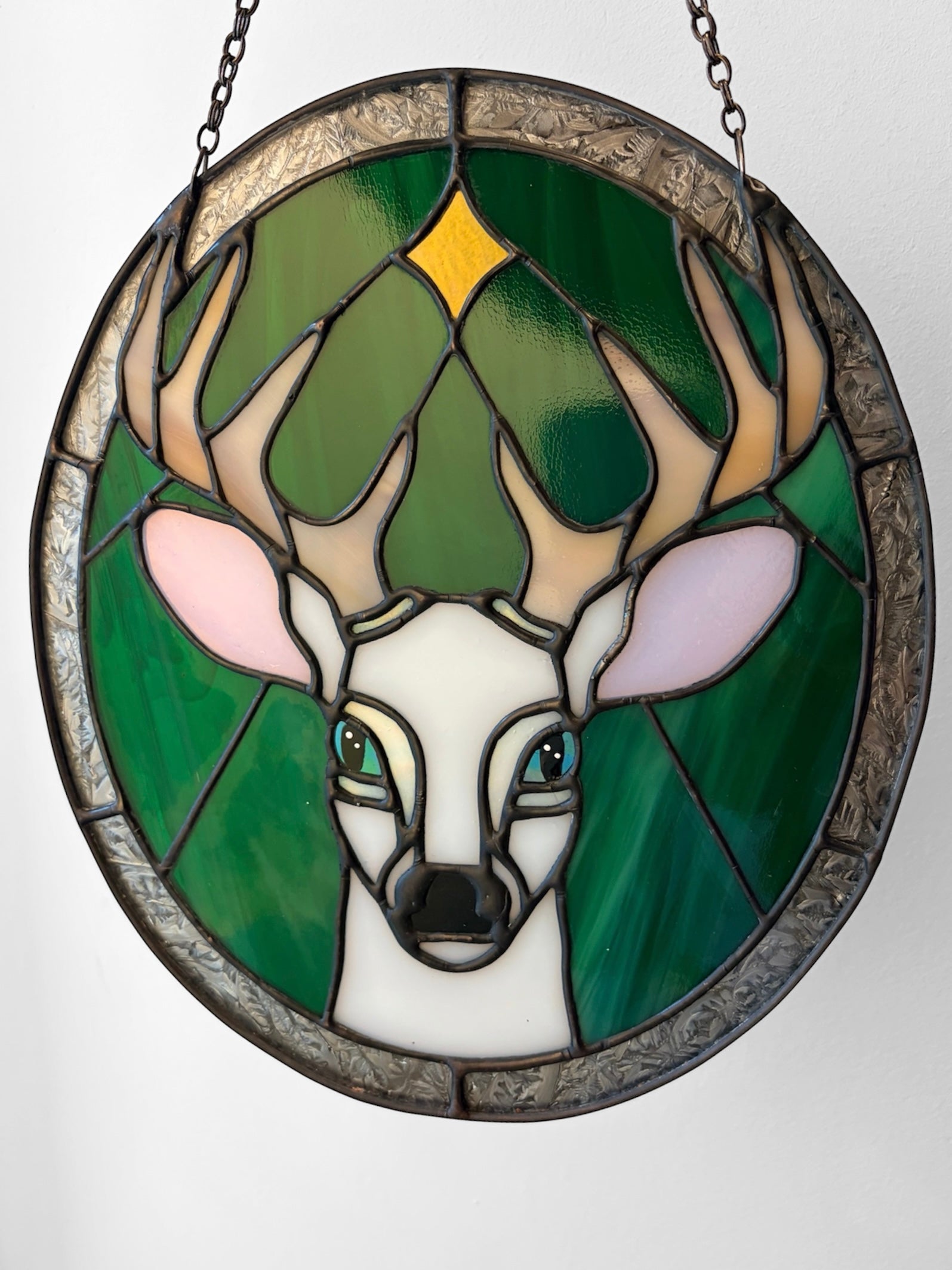 A stained glass panel picturing a white stag under a star, against a green and silver background