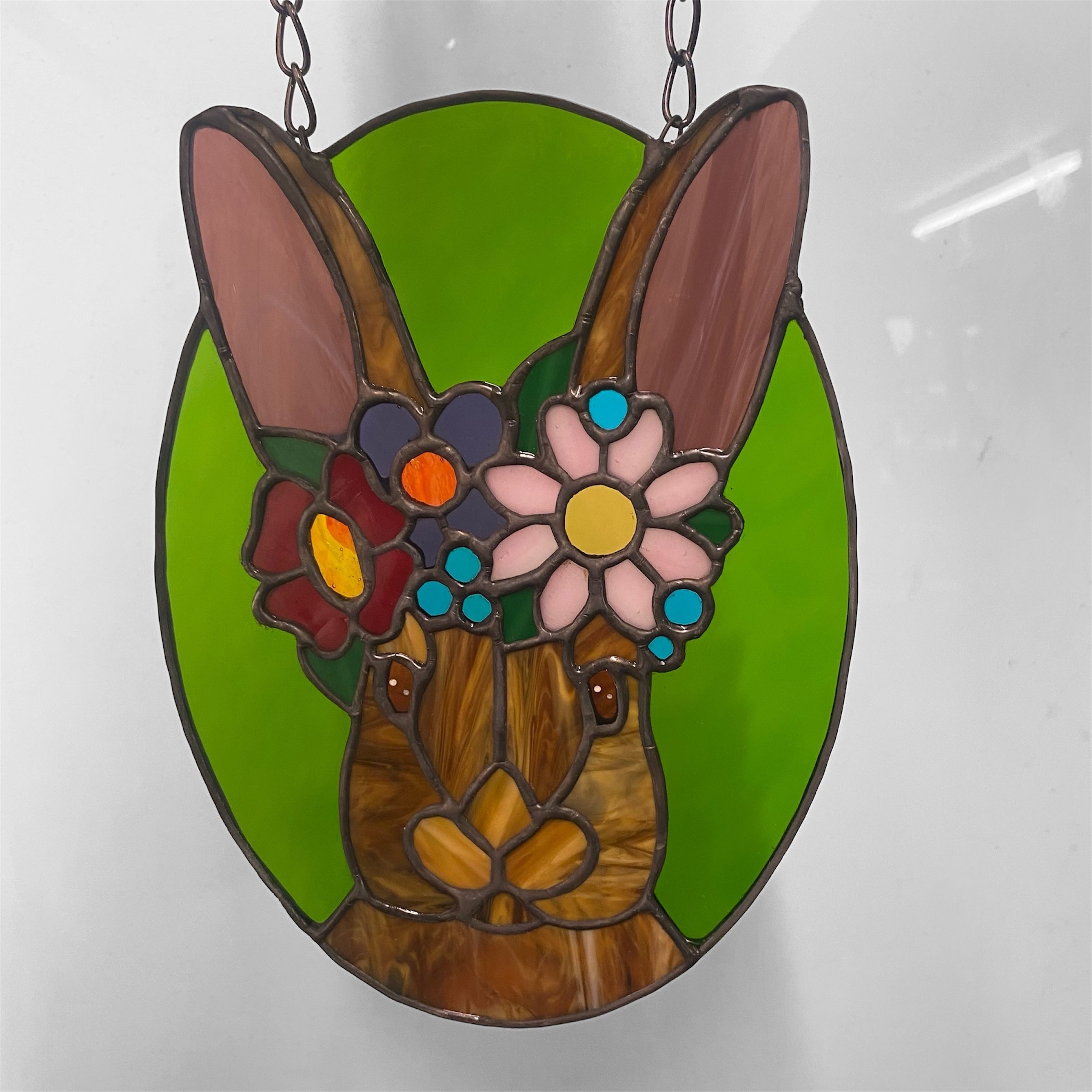 Stained glass window hanging of a rabbit with a flower crown on a white background