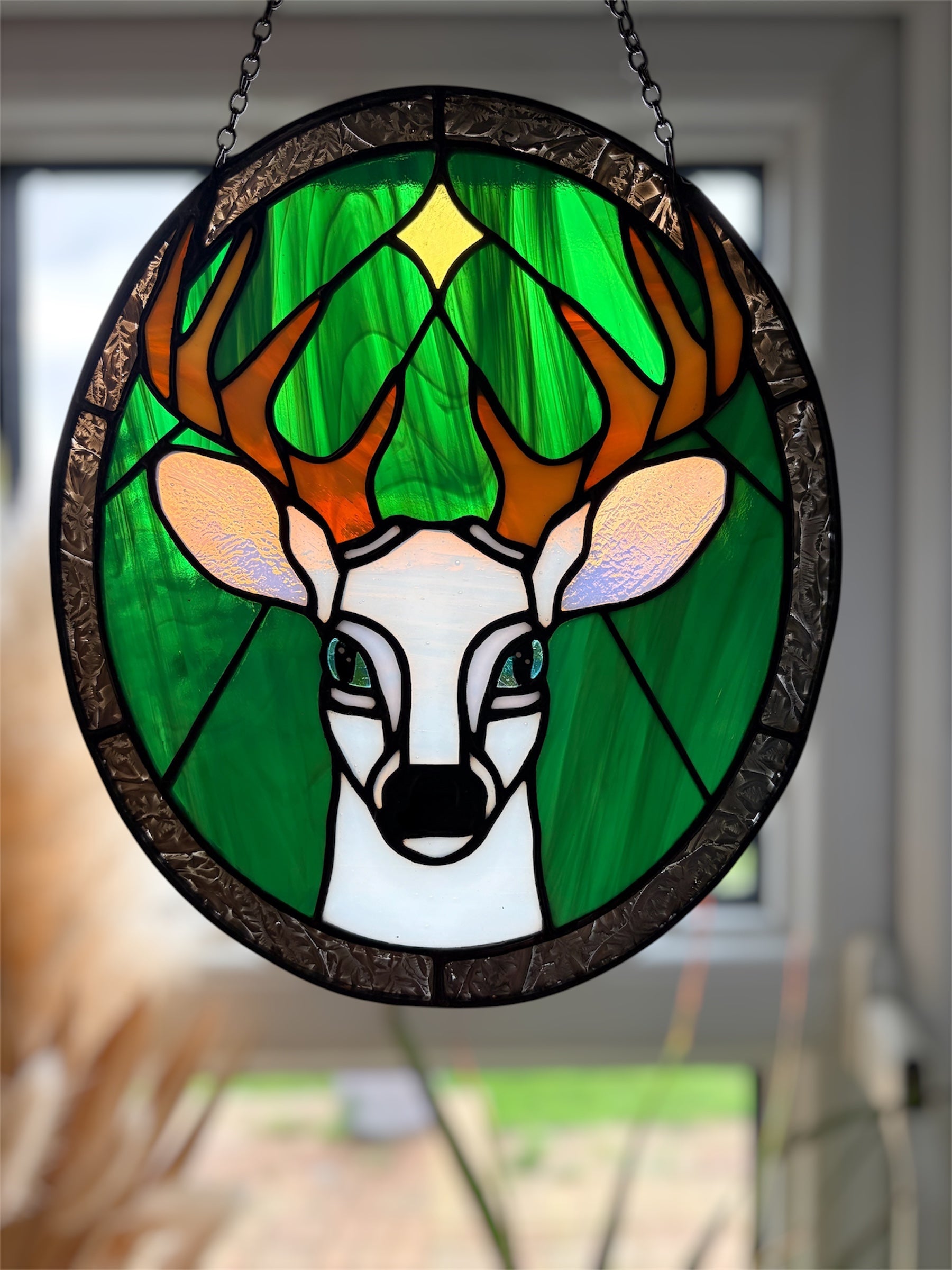 Stained glass window hanging with deer design in a home setting showing appearance when backlit