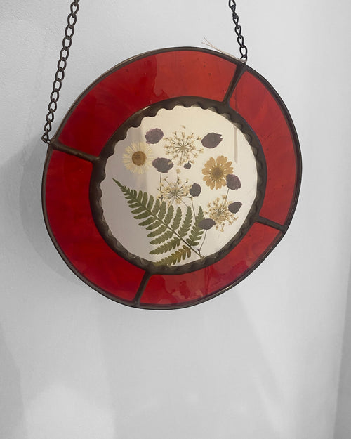 Round stained glass panel with floral design and red border on a white background