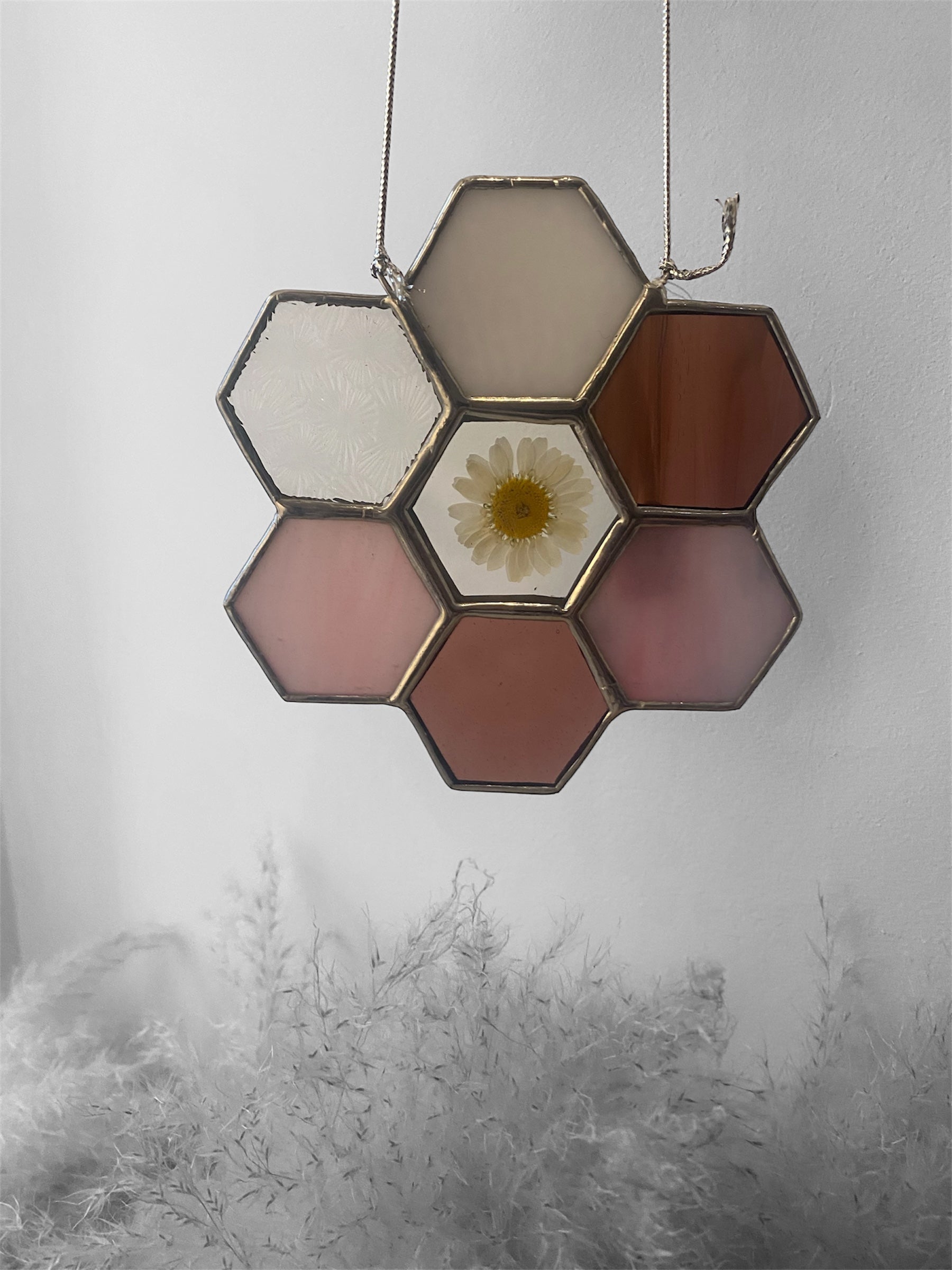Hexagonal pink stained glass panel with a central floral daisy design on a plain background