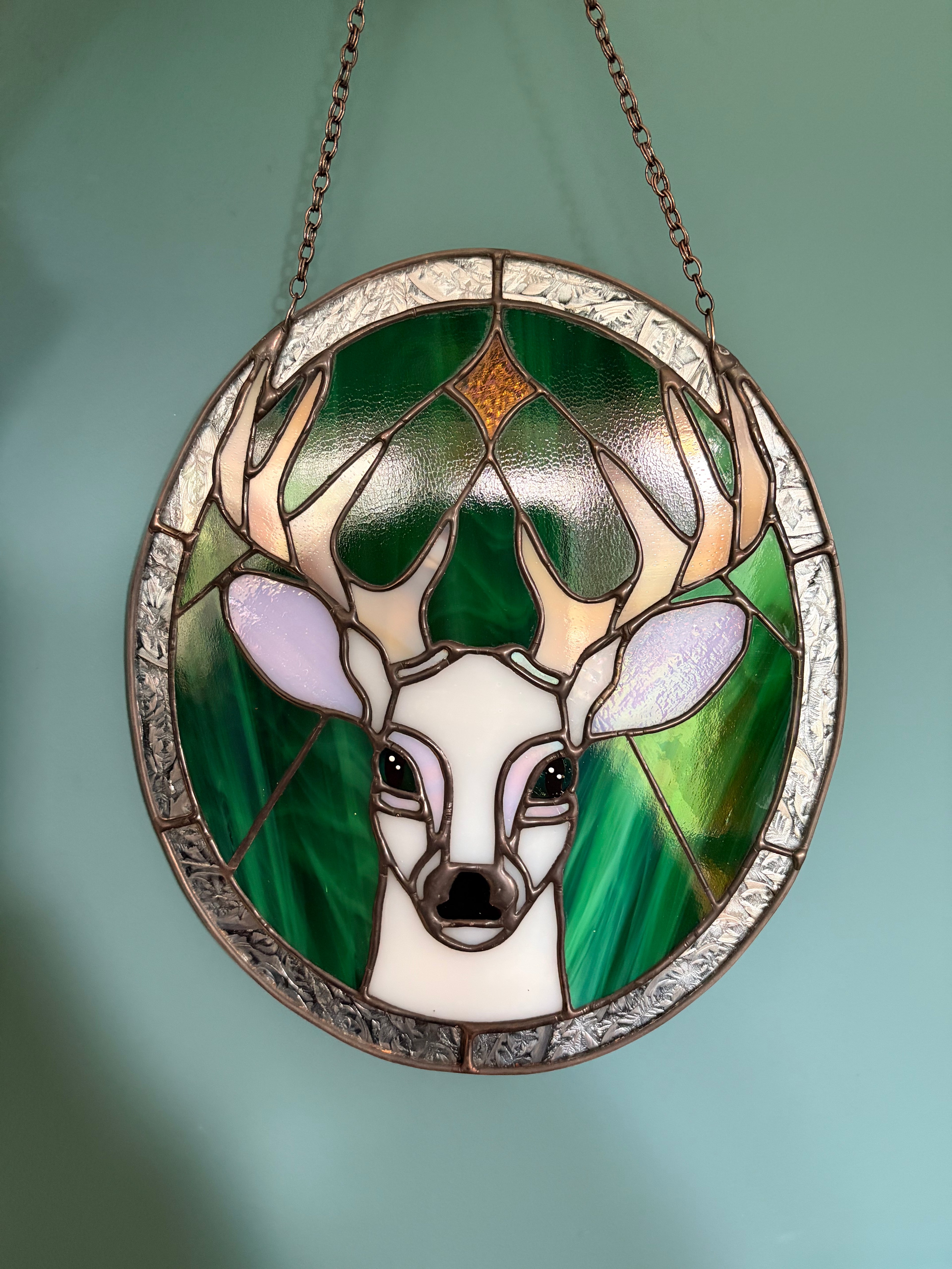 A stained glass panel picturing a white stag under a star, against a green and silver background